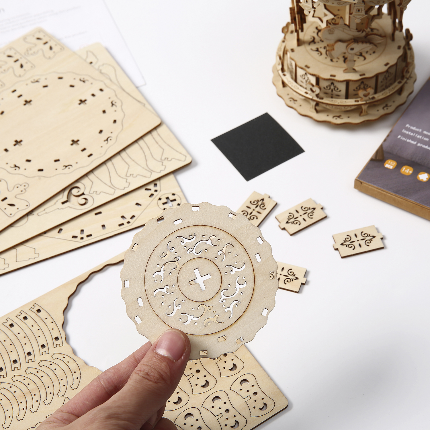 Kit modello di giostra in legno con parti, un quadrato nero e istruzioni.