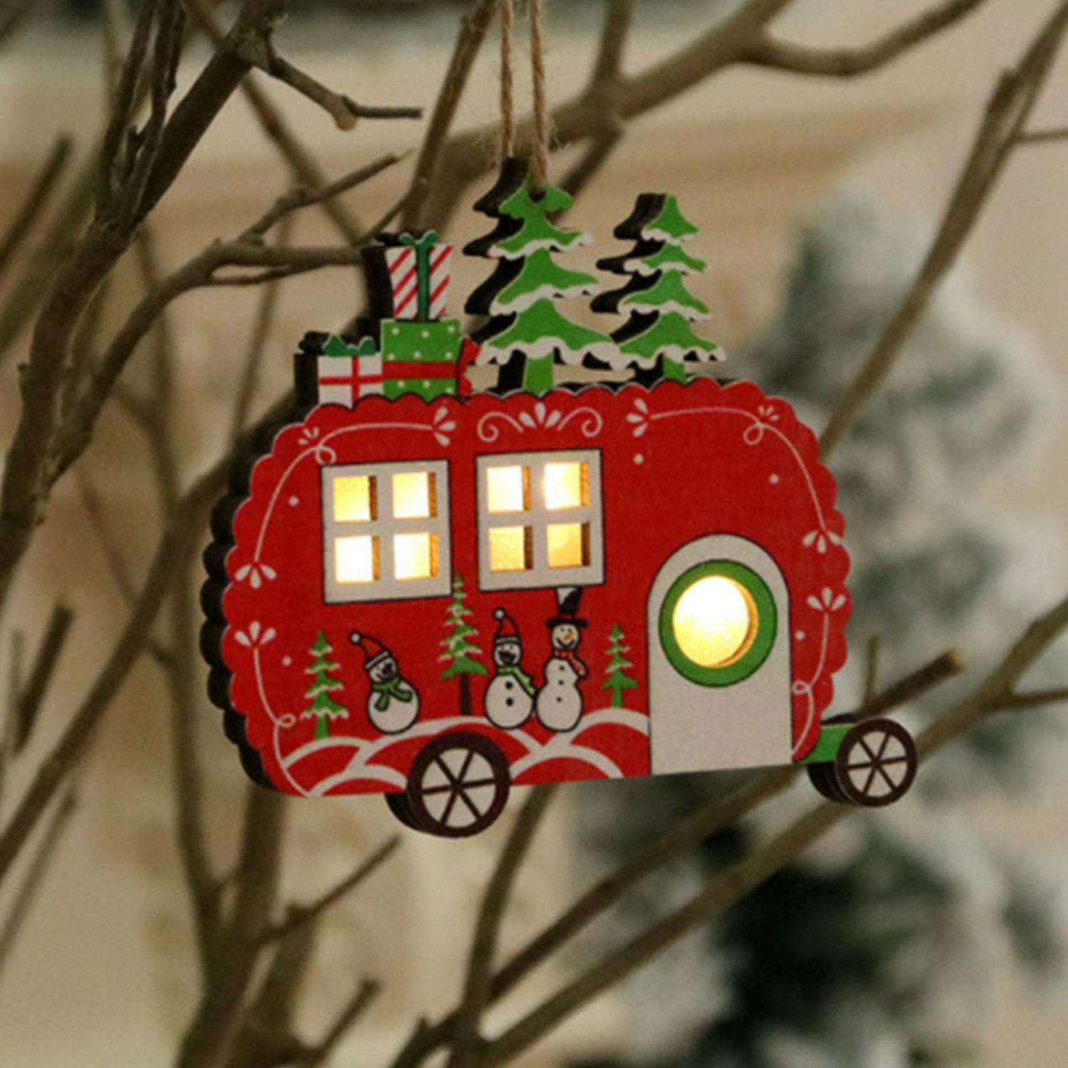 Un ornamento natalizio in legno di una roulotte rossa con pupazzi di neve, alberi, regali e finestre illuminate.