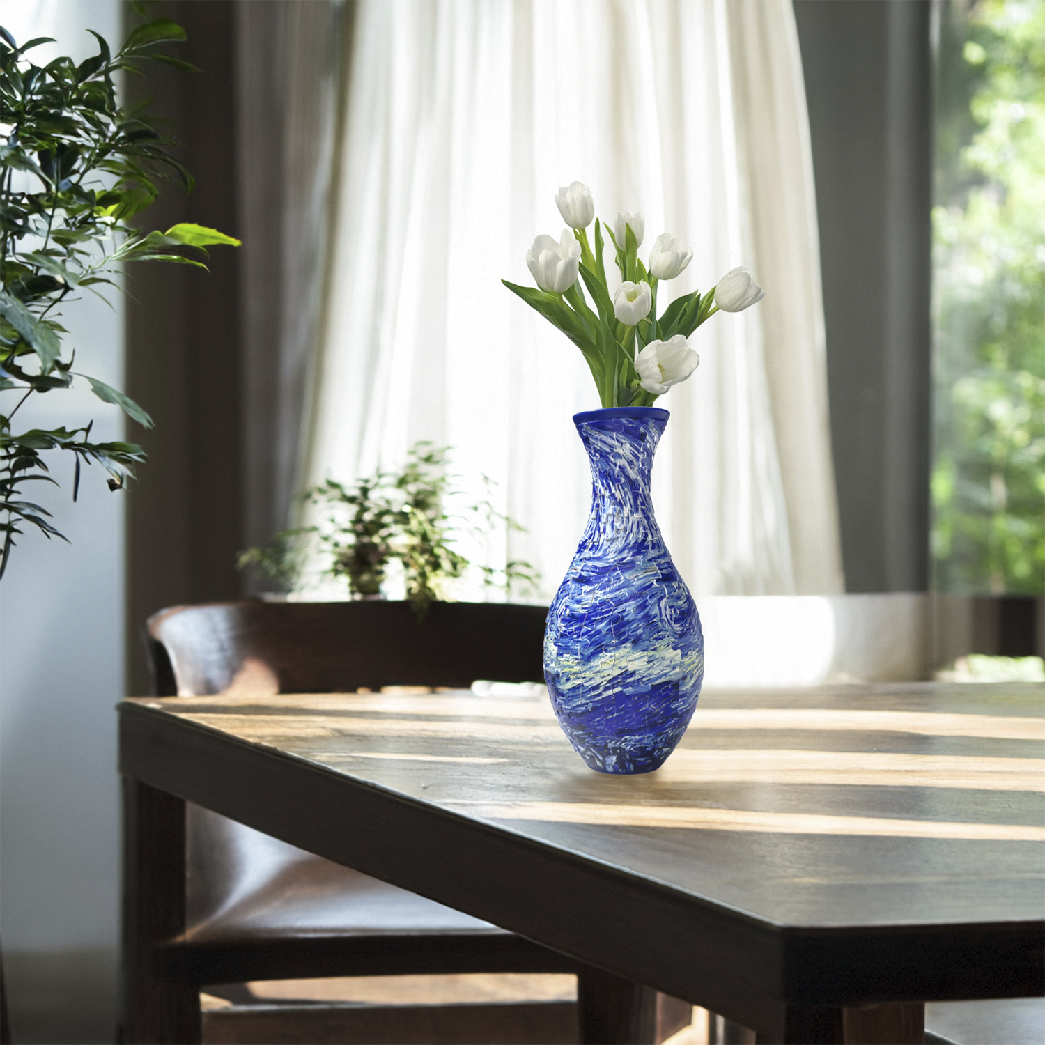 Un vaso blu vorticoso con tulipani bianchi su un tavolo di legno vicino a una finestra.