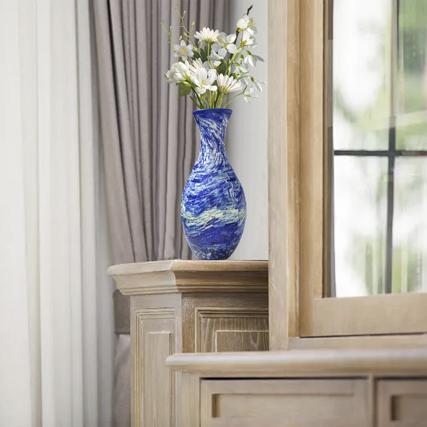 Un vaso blu in vetro di Murano con fiori bianchi poggia su un mobile in legno.