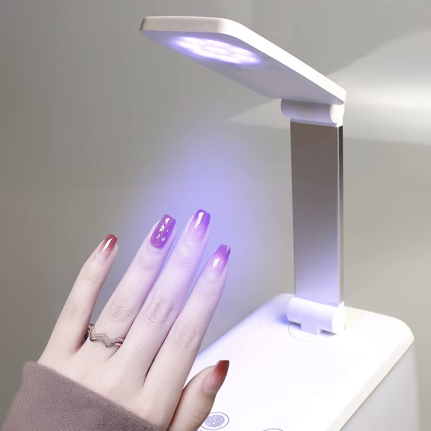Una mano con uñas moradas bajo una lámpara UV, curando.