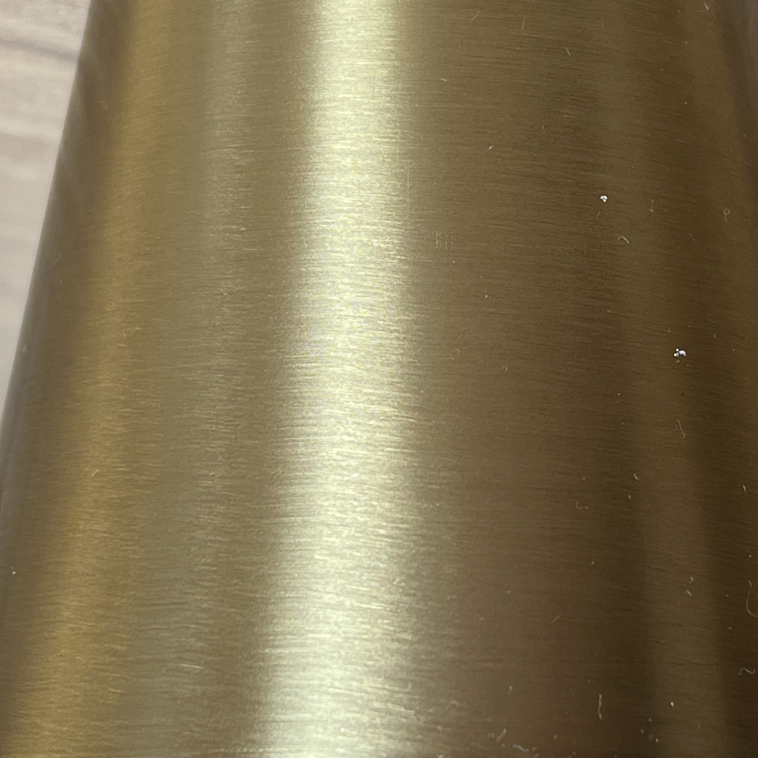 Goldfarbene Metalloberfläche mit horizontalen Bürstenstrichen und Lichtreflexionen.