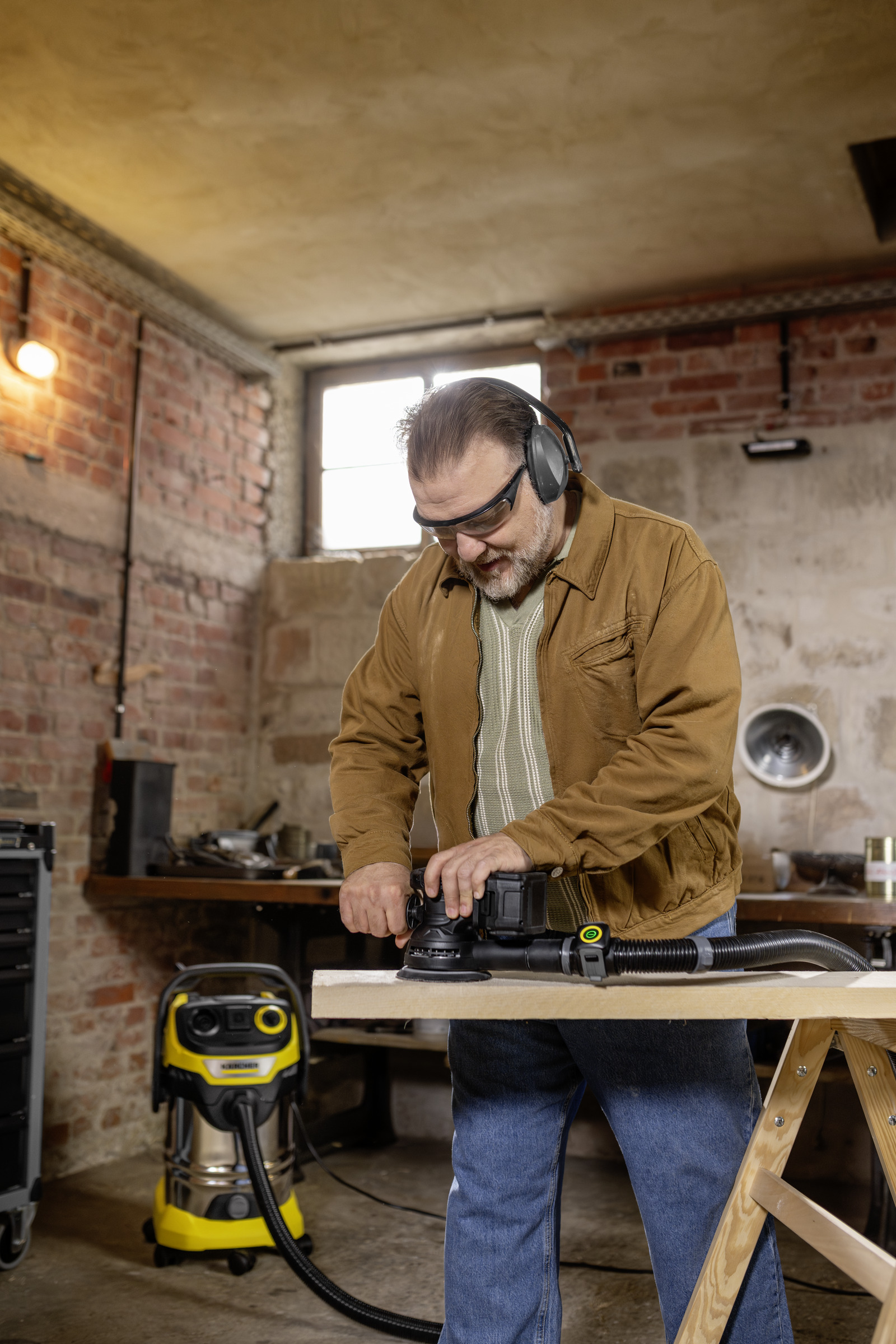 Mann schleift Holz in Werkstatt mit Schutzbrille und Kopfhörern.