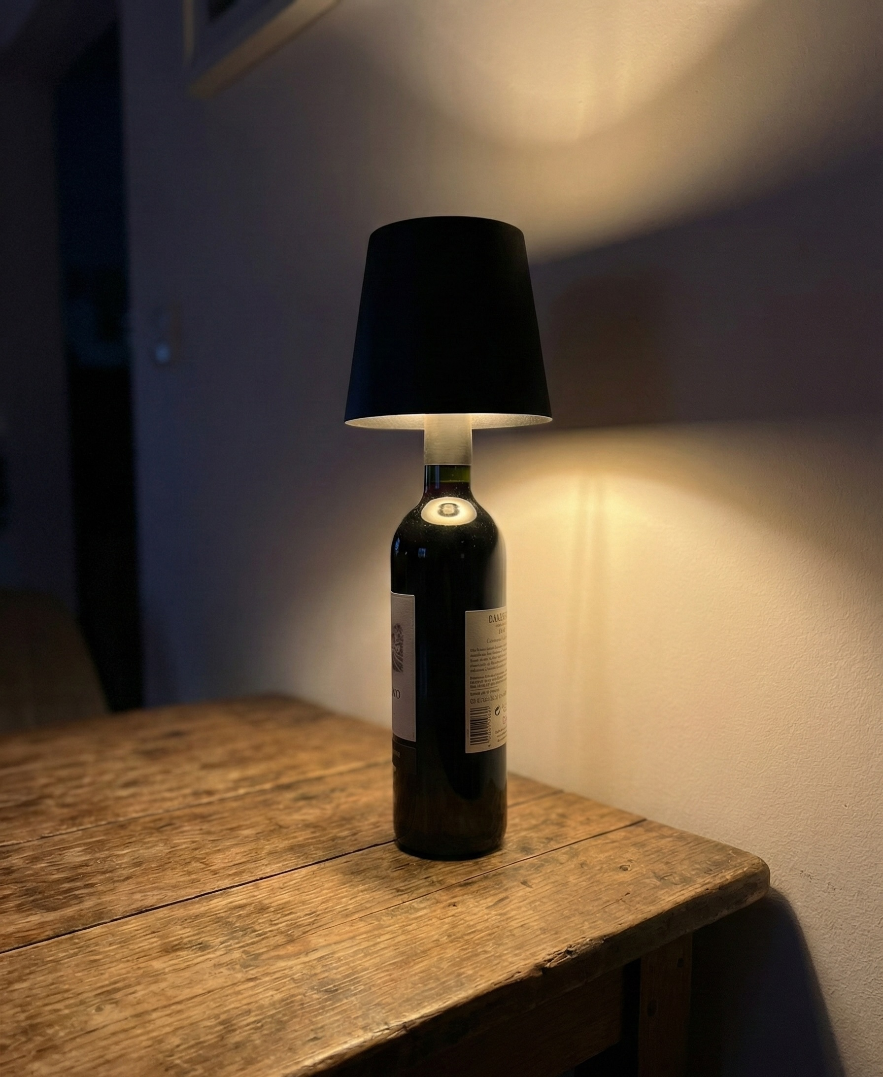 Eine Lampe mit schwarzem Schirm auf einer Weinflasche auf einem Holztisch.