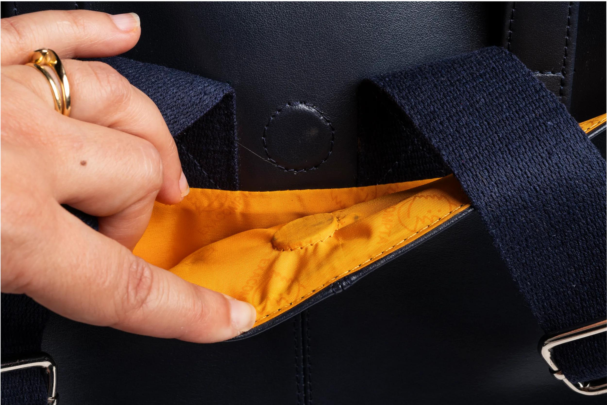Mano con anillo dorado abre bolso azul oscuro con forro naranja.