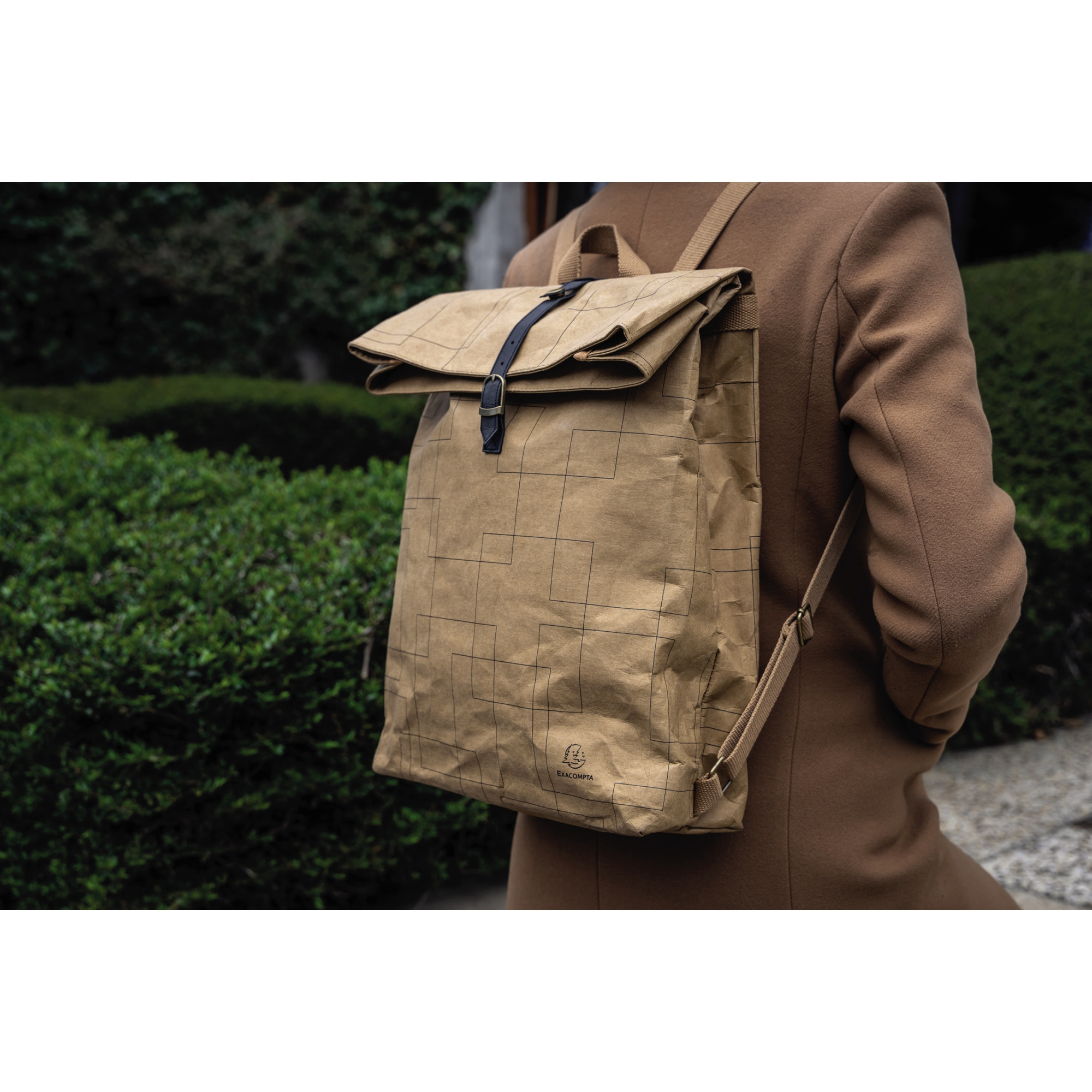 Persona con abrigo marrón y mochila de papel con estampado de rejilla.