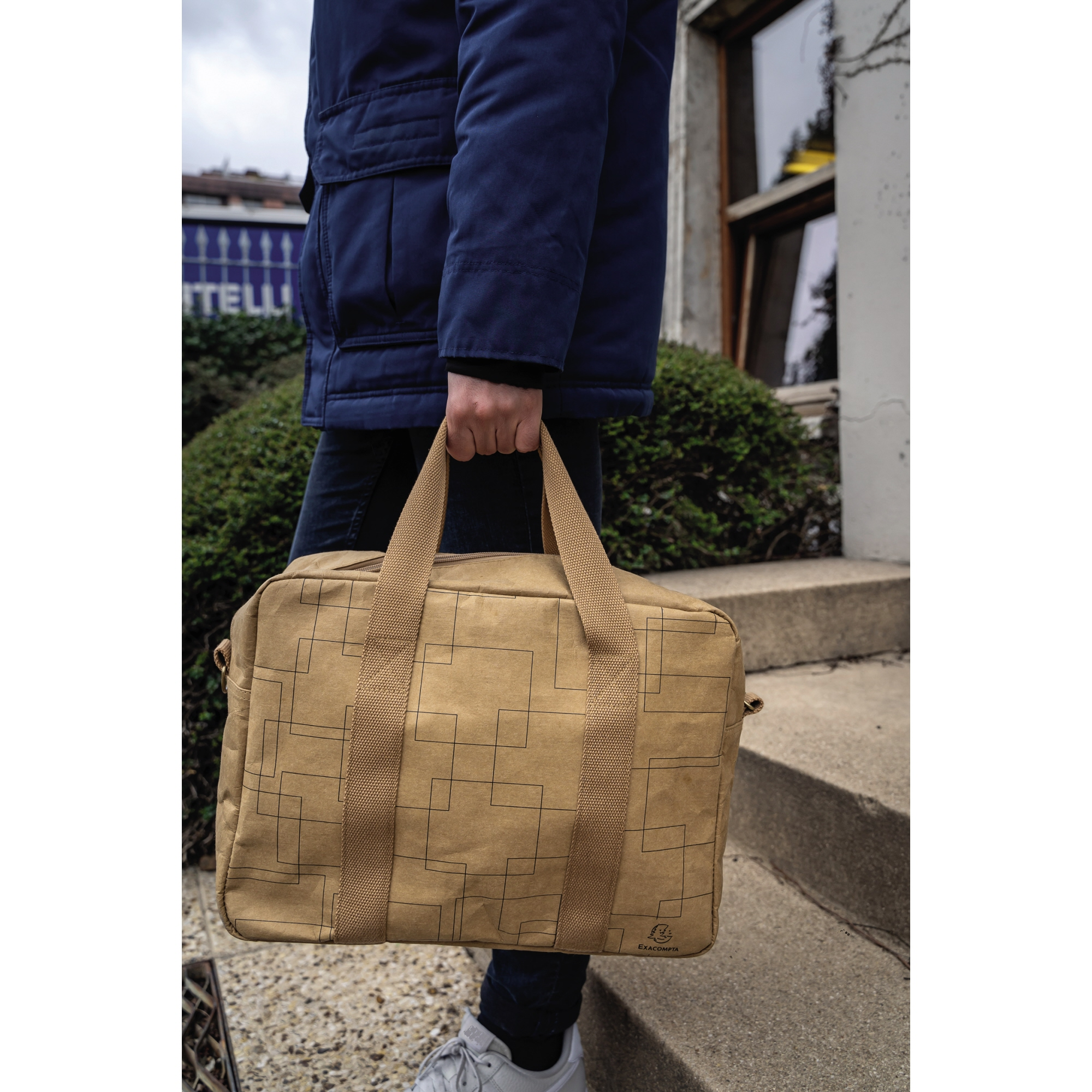 Persona con chaqueta azul sostiene bolsa marrón con patrón de rejilla.