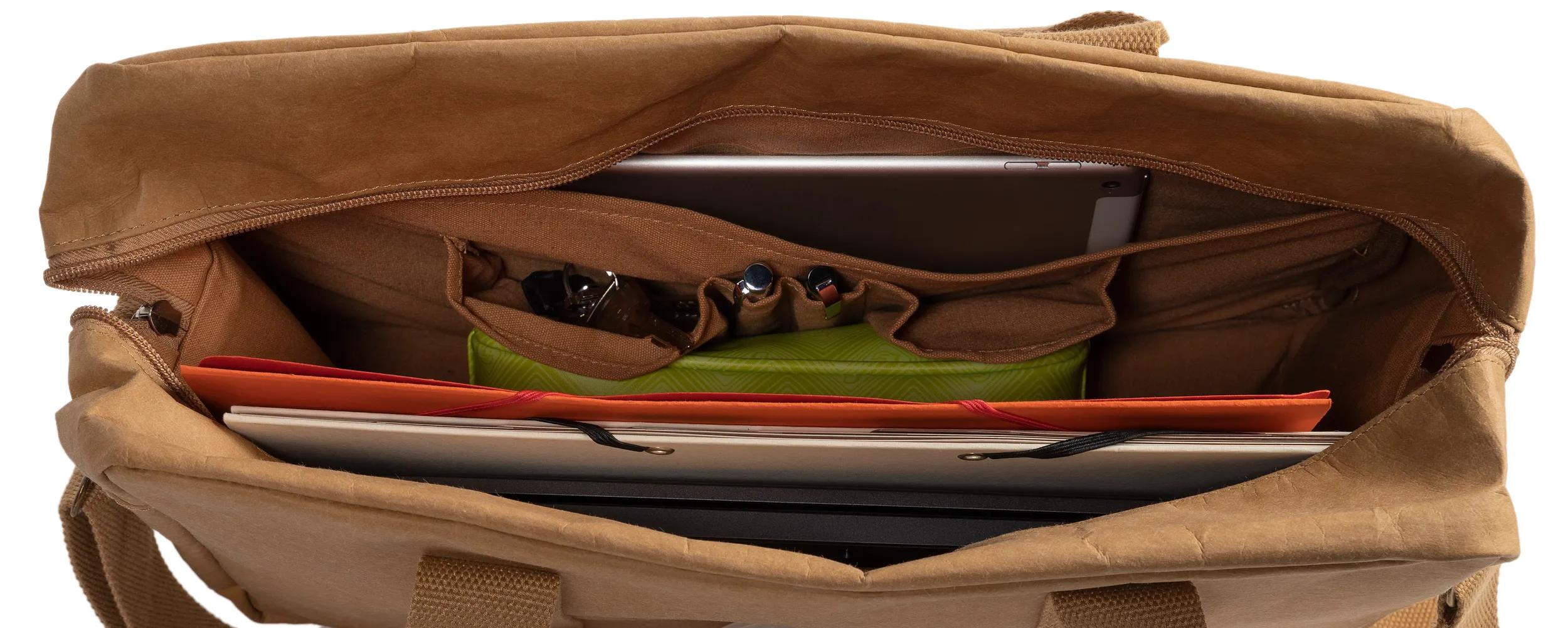 Una bolsa marrón con una tableta, libros, bolígrafos y una lata verde.