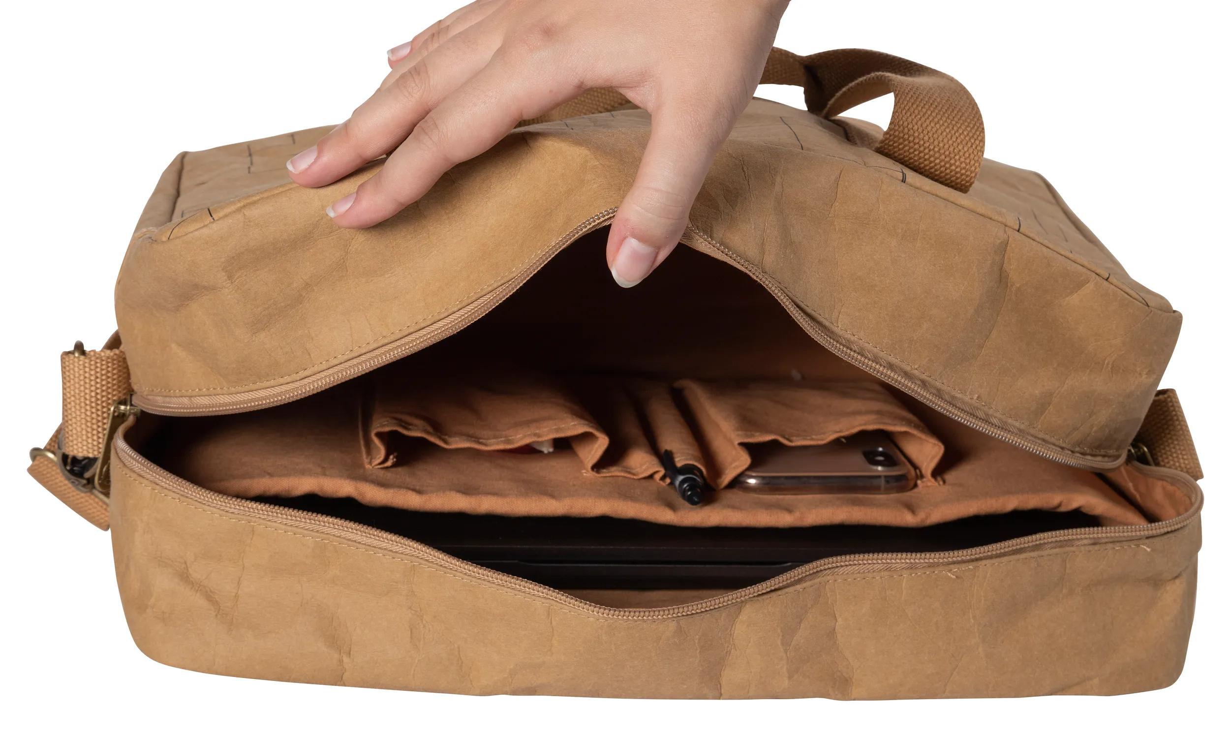 Una mano abre una bolsa marrón. Dentro hay un teléfono y bolígrafos.