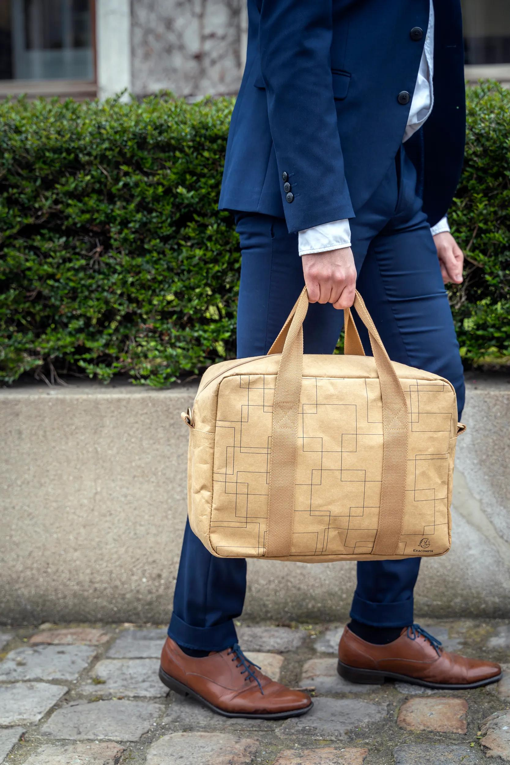 Hombre con traje azul lleva bolso marrón con patrón geométrico.
