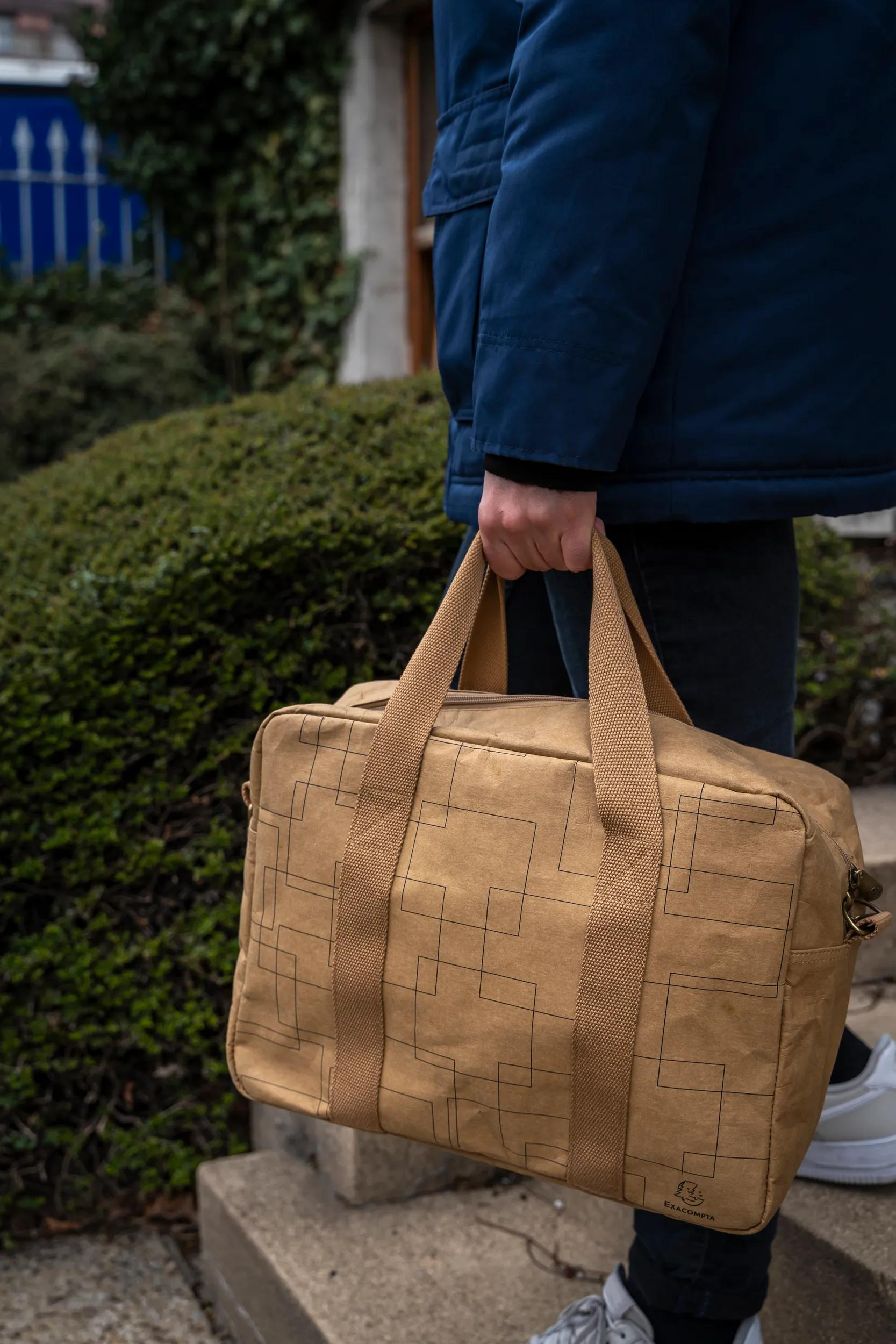 Persona con chaqueta azul lleva bolso marrón con patrón geométrico.