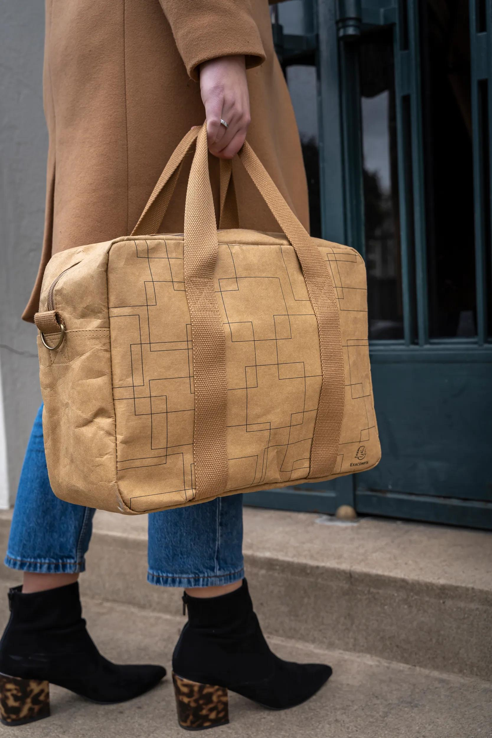 Una persona lleva un bolso marrón con patrón de rejilla, jeans y botas negras.