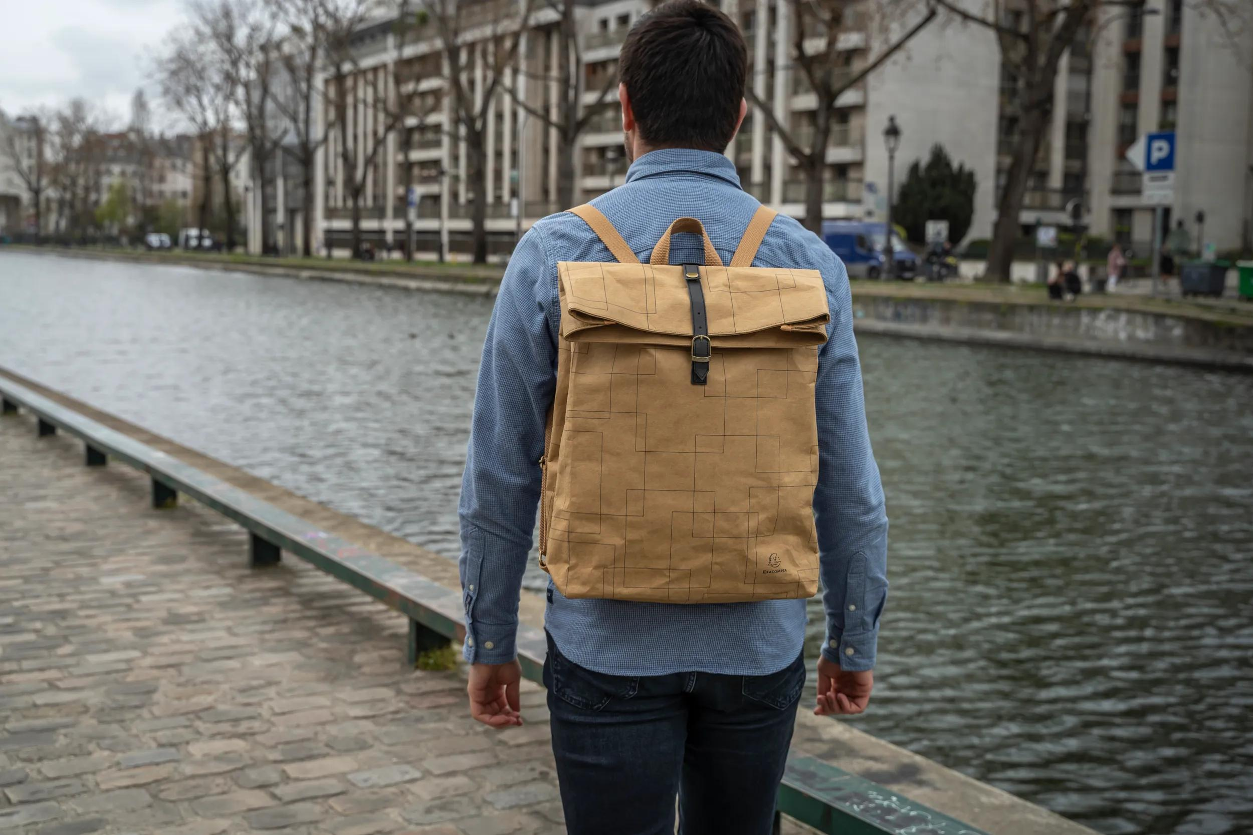 Hombre con mochila marrón y camisa azul camina por un canal.