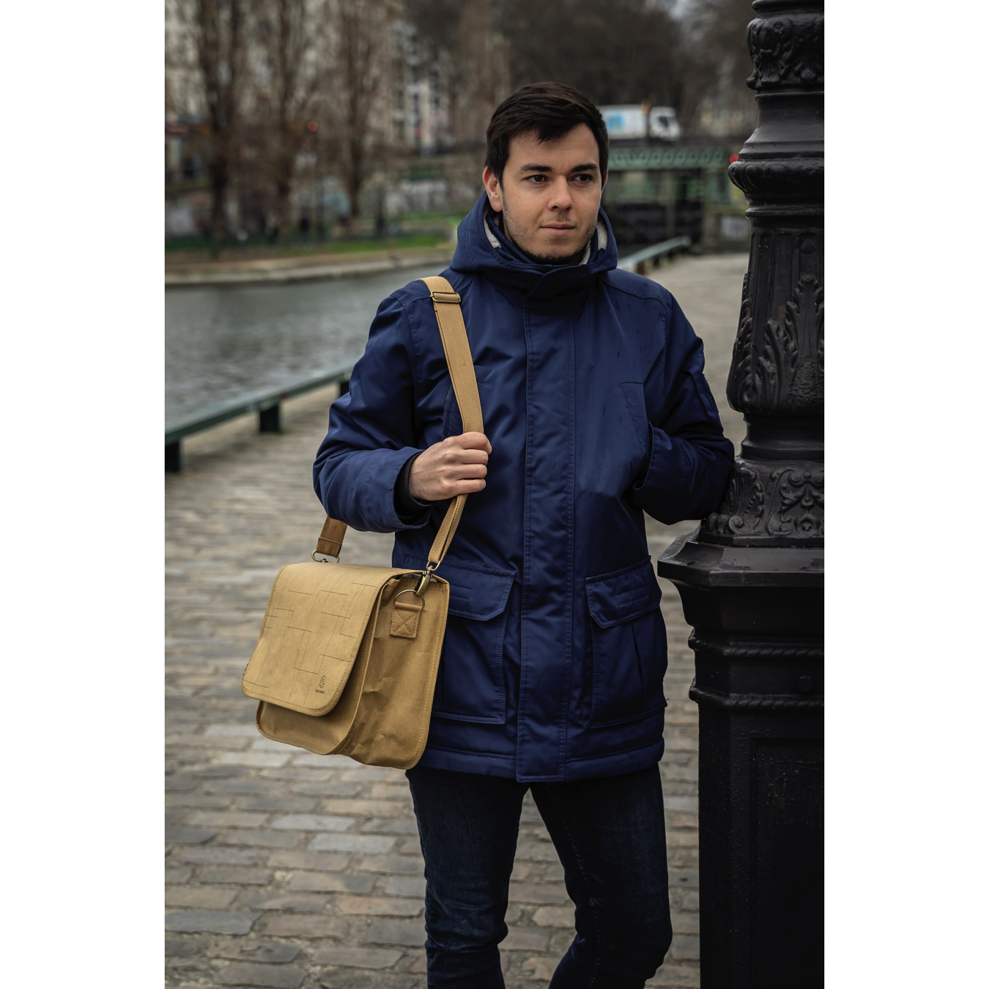Un hombre con chaqueta azul y bolso cruzado está junto a una farola.
