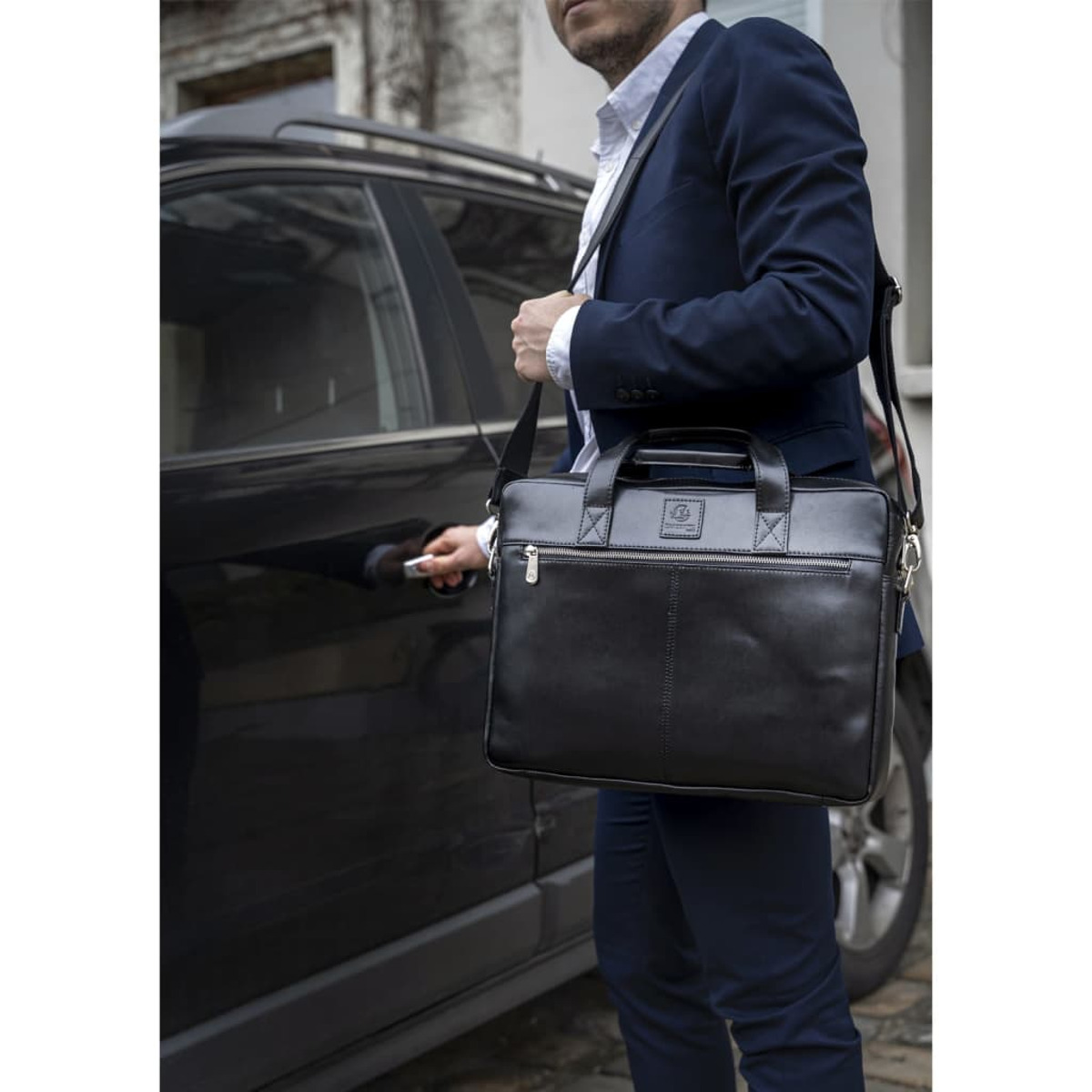Hombre con traje azul marino abre puerta de coche, lleva maletín negro.