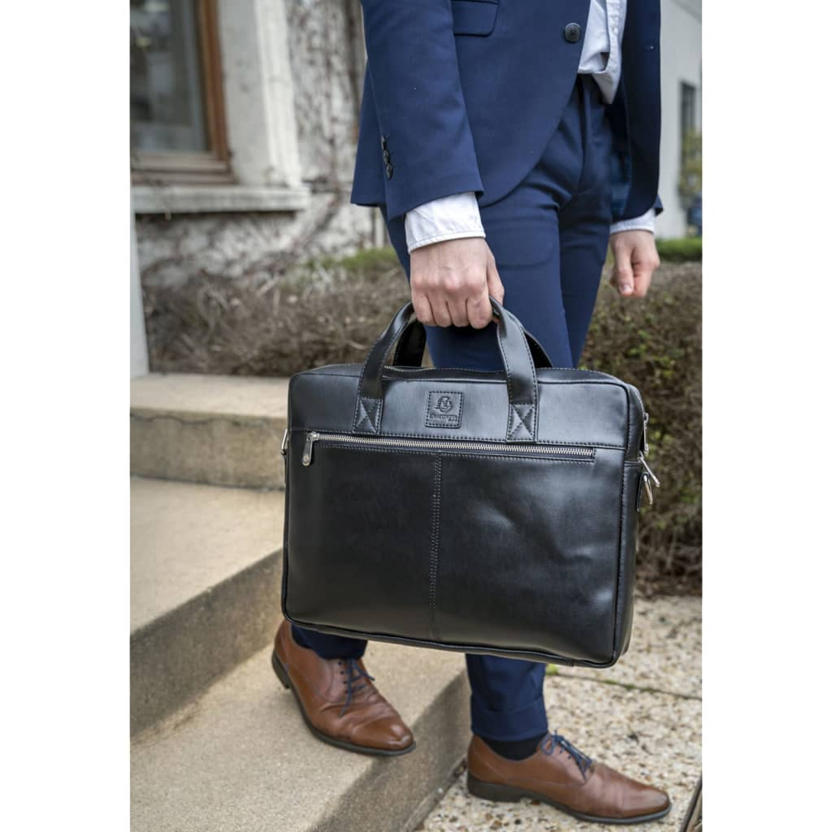 Hombre con traje azul marino, maletín negro y zapatos marrones en escalones de piedra.