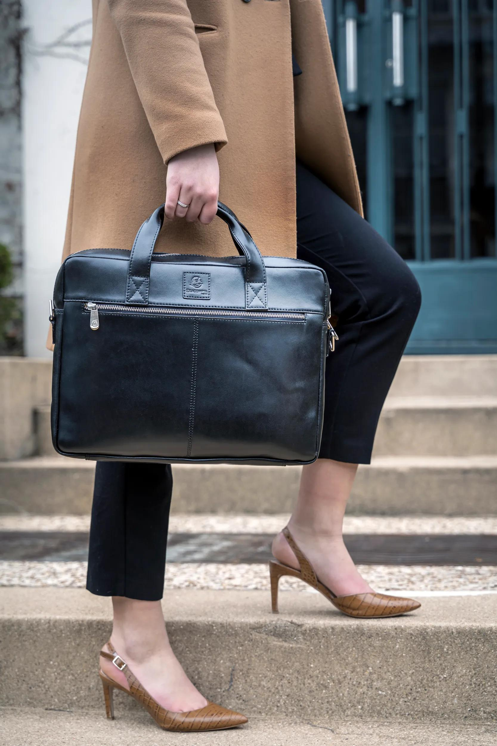 Mujer con abrigo marrón, pantalones negros, tacones y bolso negro en escaleras.
