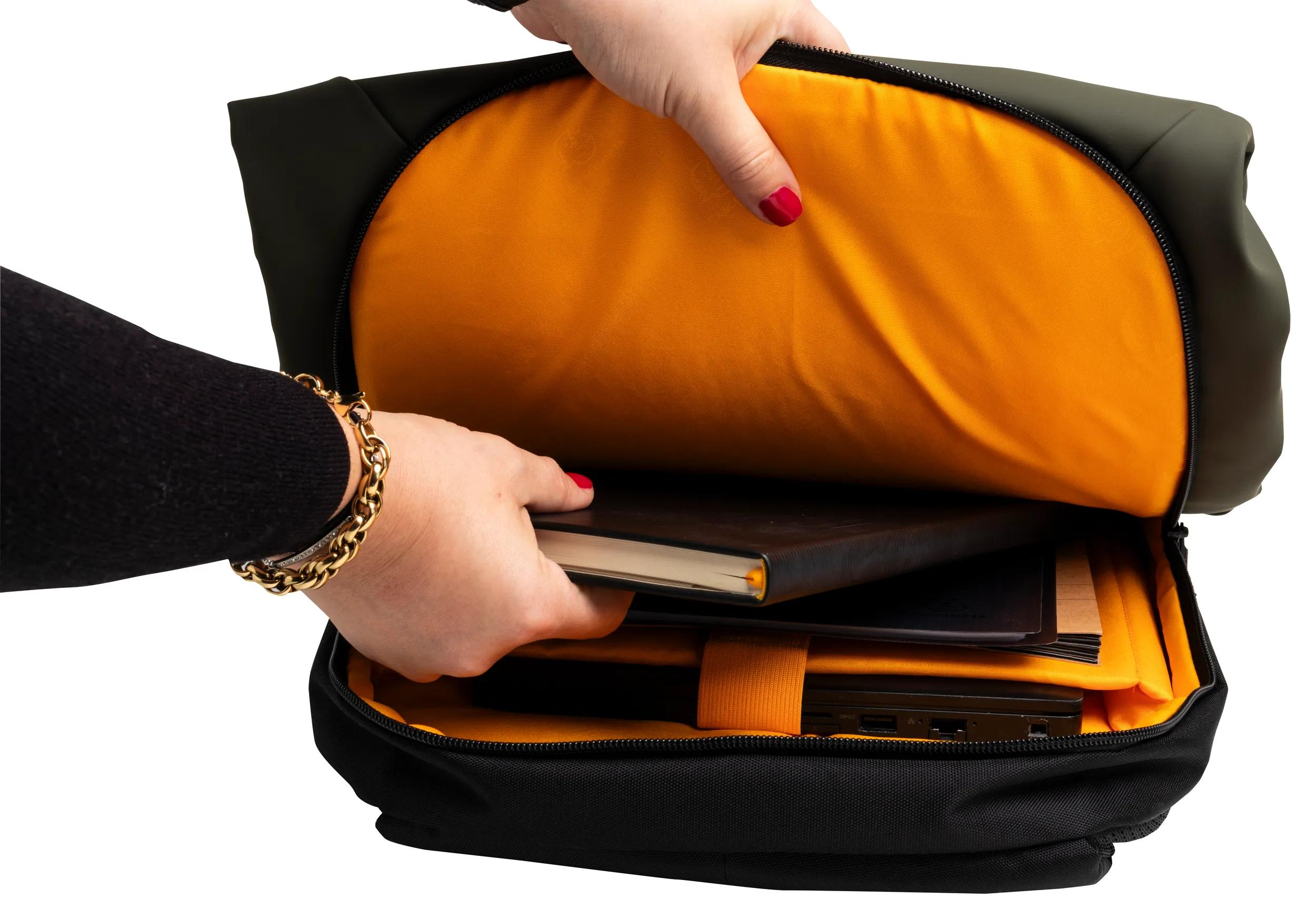 Una mano coloca un cuaderno en una mochila negra con forro interior naranja.