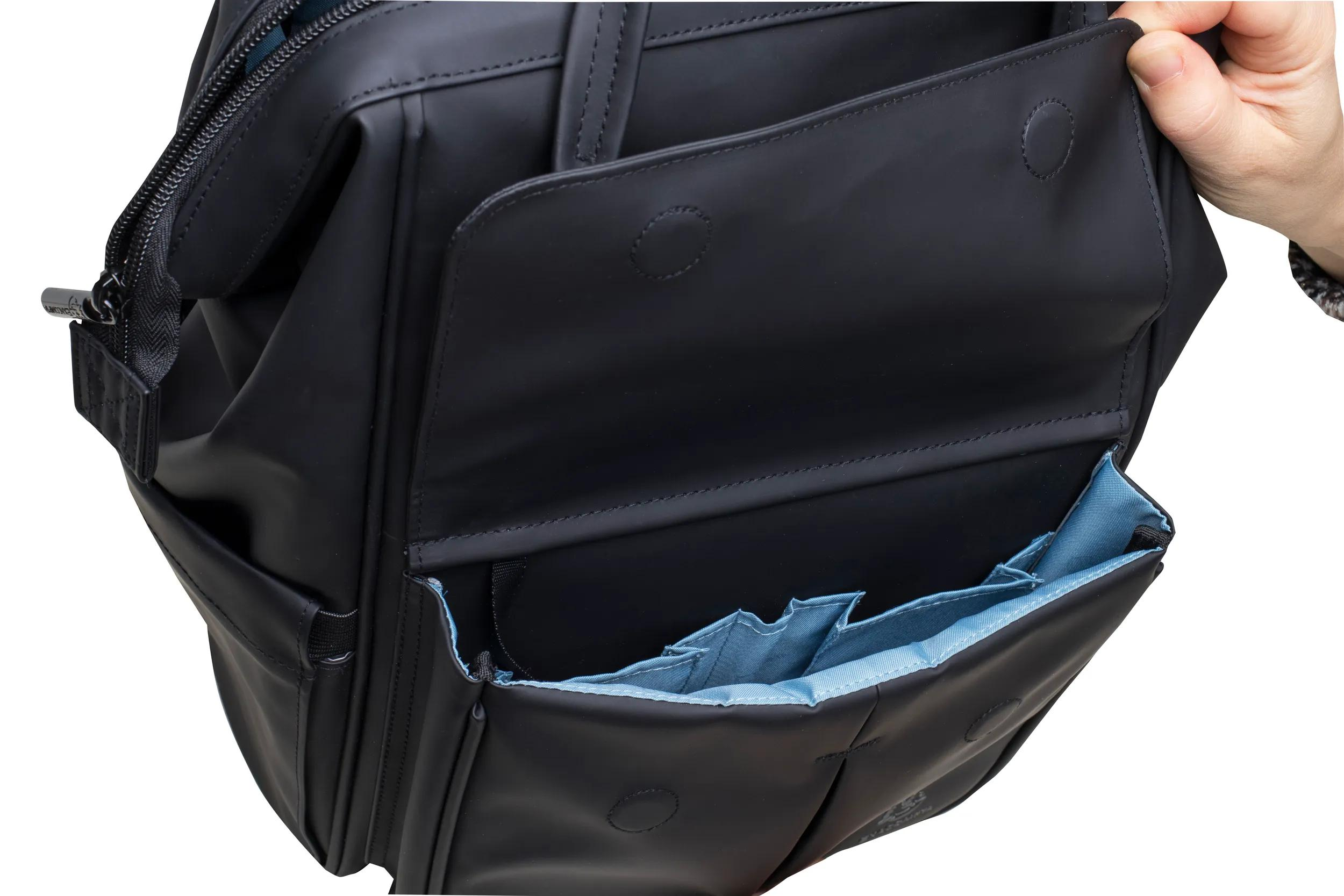 Una mano abre un bolso negro con interior azul claro y compartimentos.