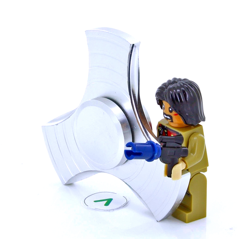 Una figura de Lego con un arma se encuentra junto a un gran spinner de fidget plateado.