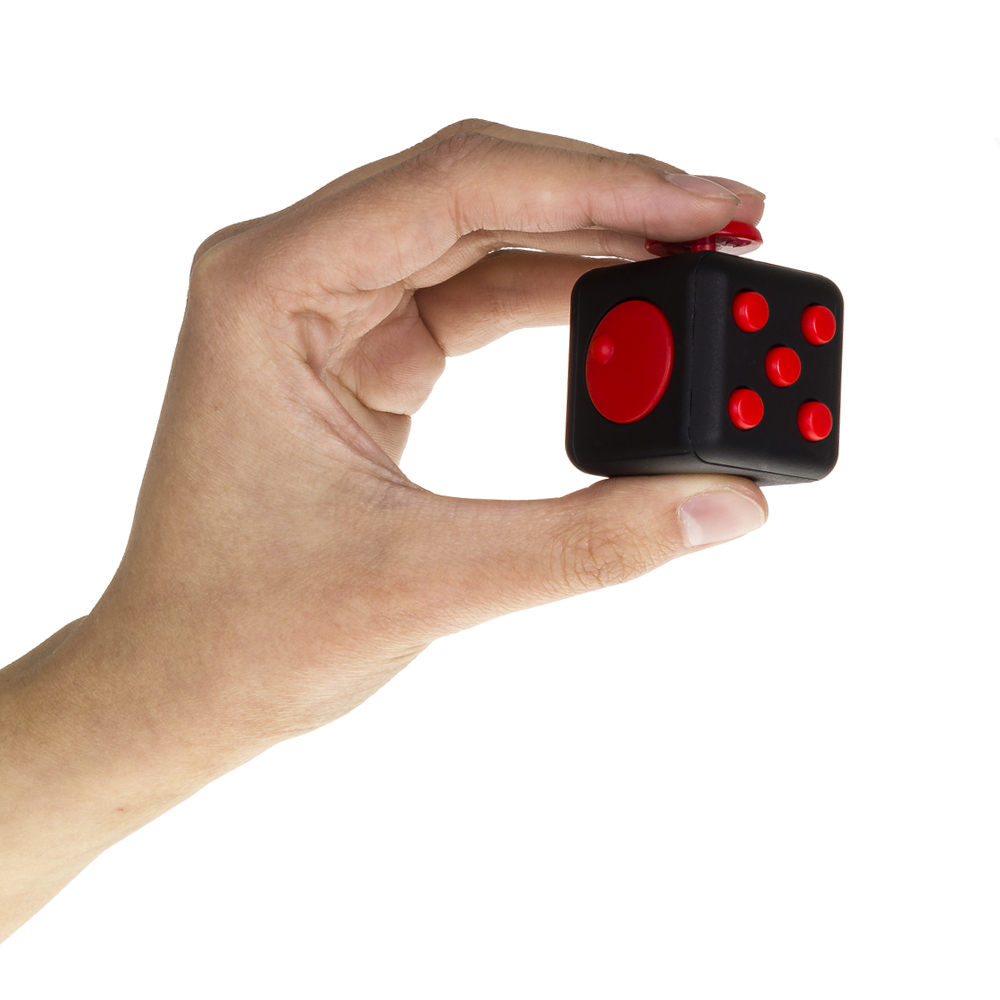Una mano sostiene un cubo negro con botones y diales rojos.