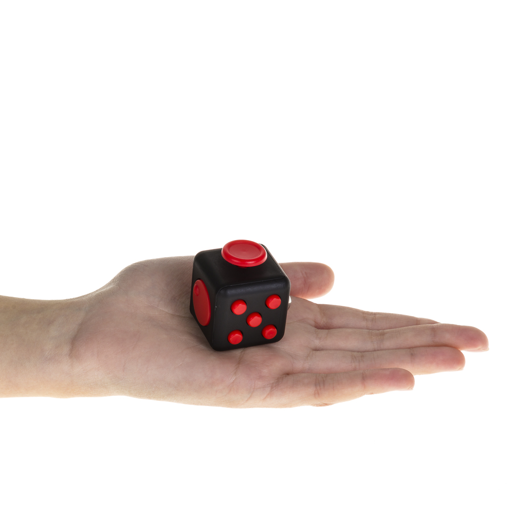 Una mano sostiene un cubo negro con botones rojos y un botón rojo arriba.