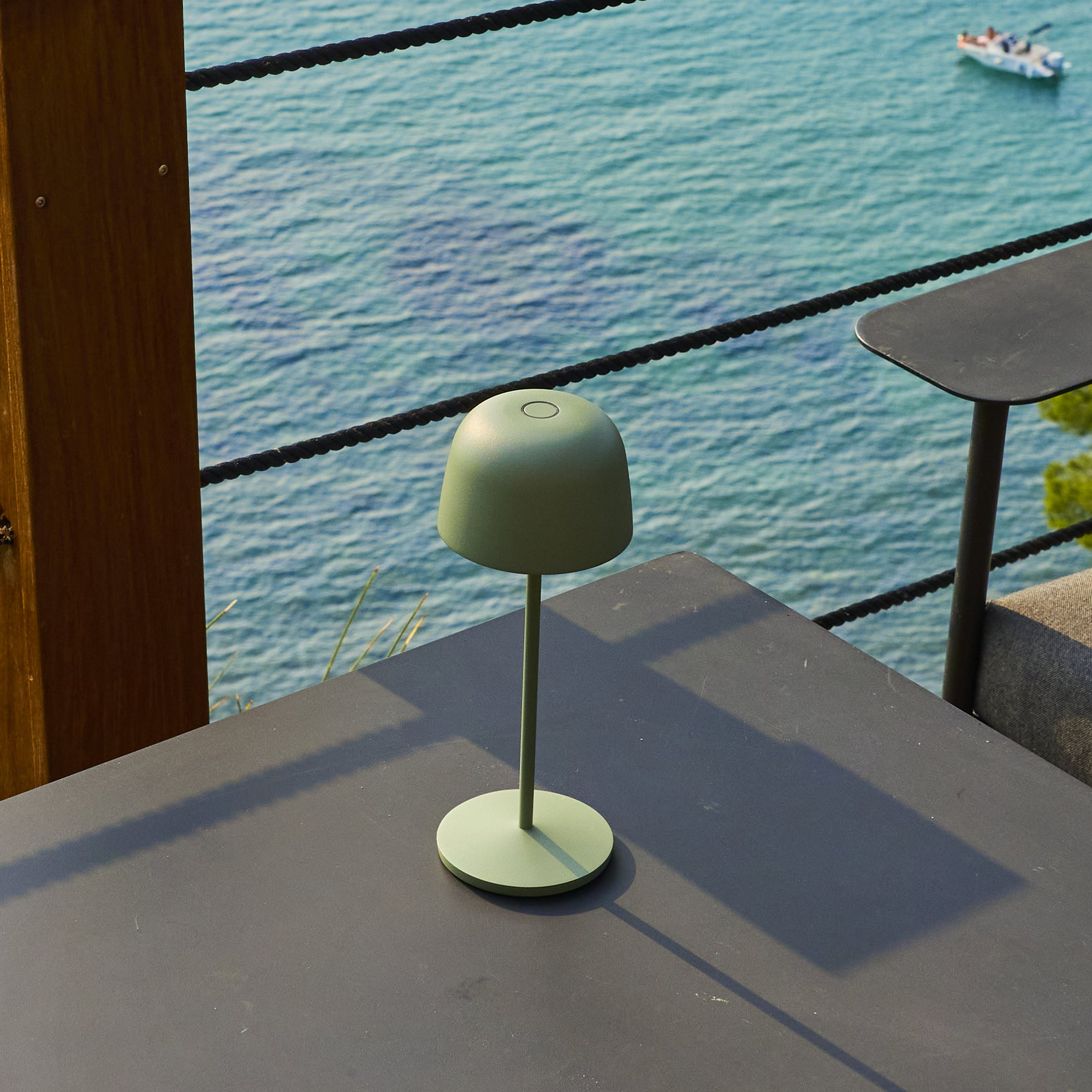 Grüne Lampe auf Tisch am Meer mit Boot im Hintergrund.