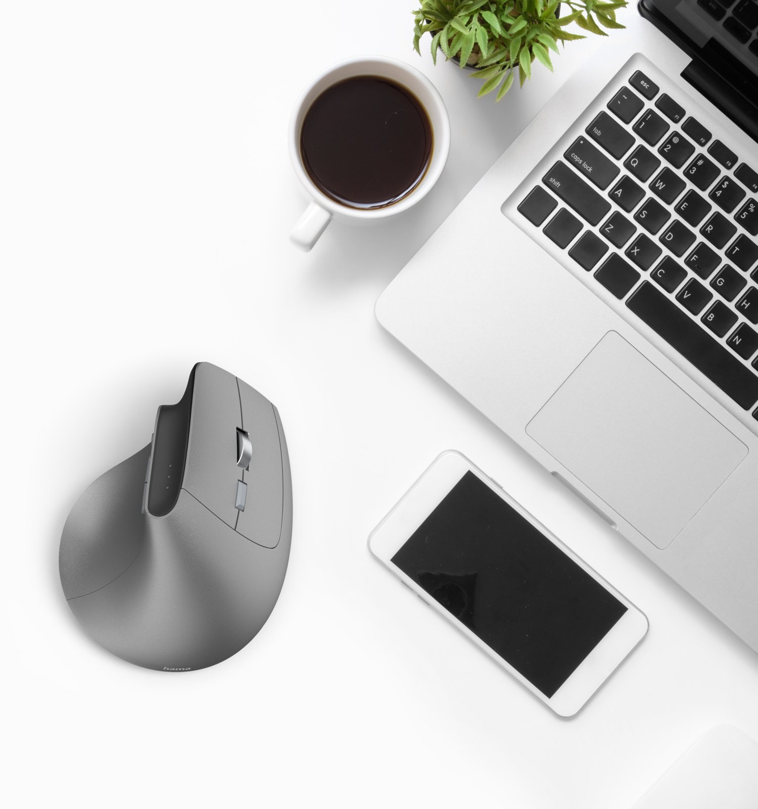 Szara mysz, filiżanka kawy, smartfon i laptop na białym biurku.