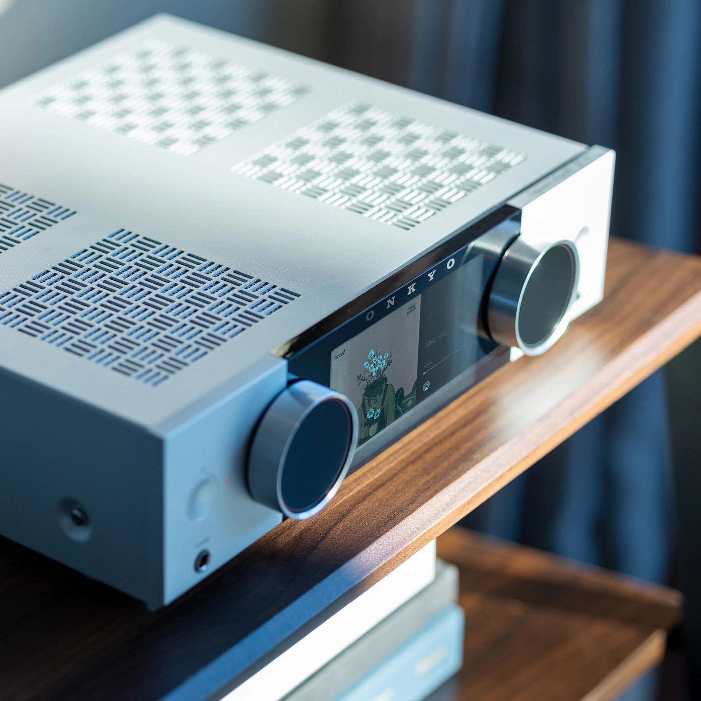 Ein silberner ONKYO-Verstärker mit digitalen Knöpfen und Bildschirm steht auf einem Holzregal.