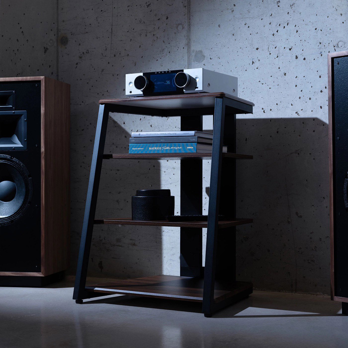 Ein moderner Hi-Fi-Receiver steht auf einem schwarzen Regal neben Lautsprechern.