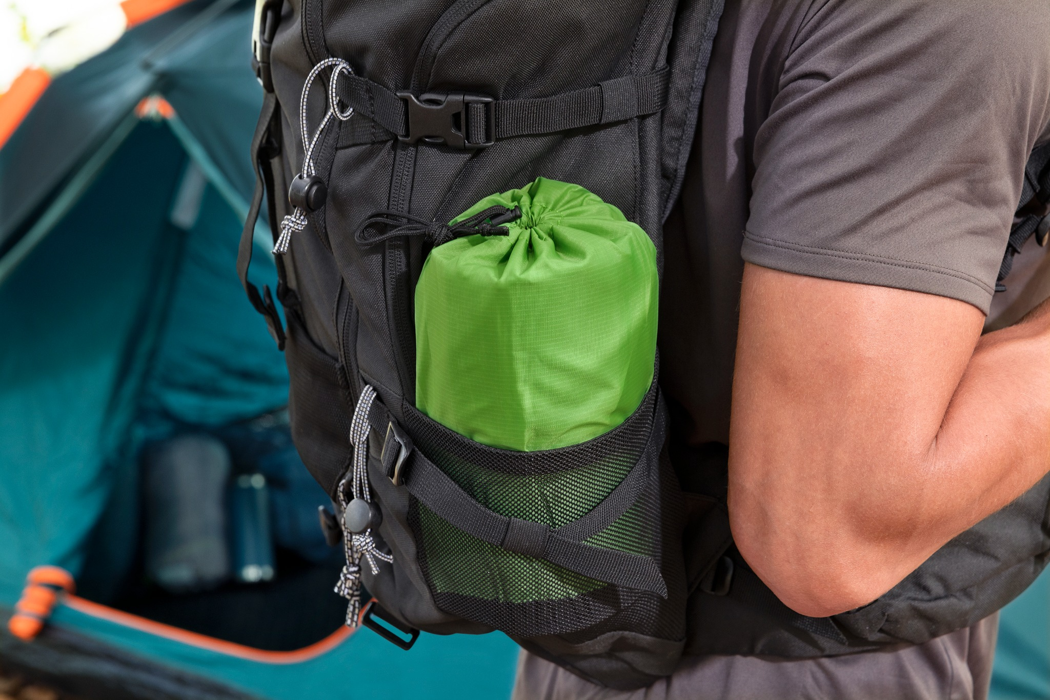 Ein Rucksack mit einer grünen Rolle und einem Zelt im Hintergrund.