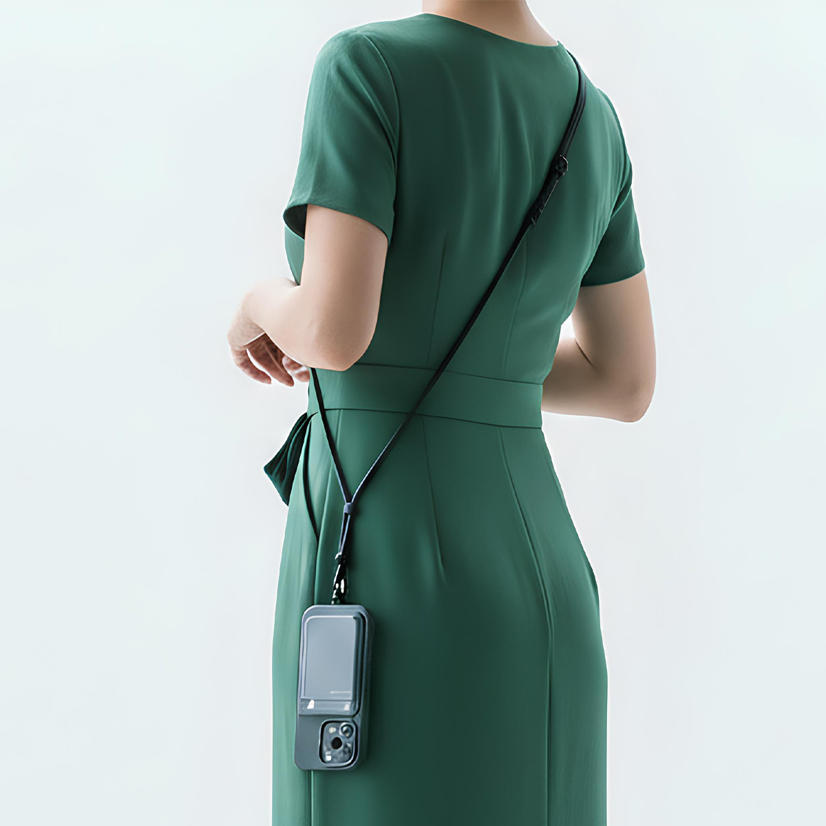 Rückansicht einer Frau im grünen Kleid mit Handy-Hülle am Träger.
