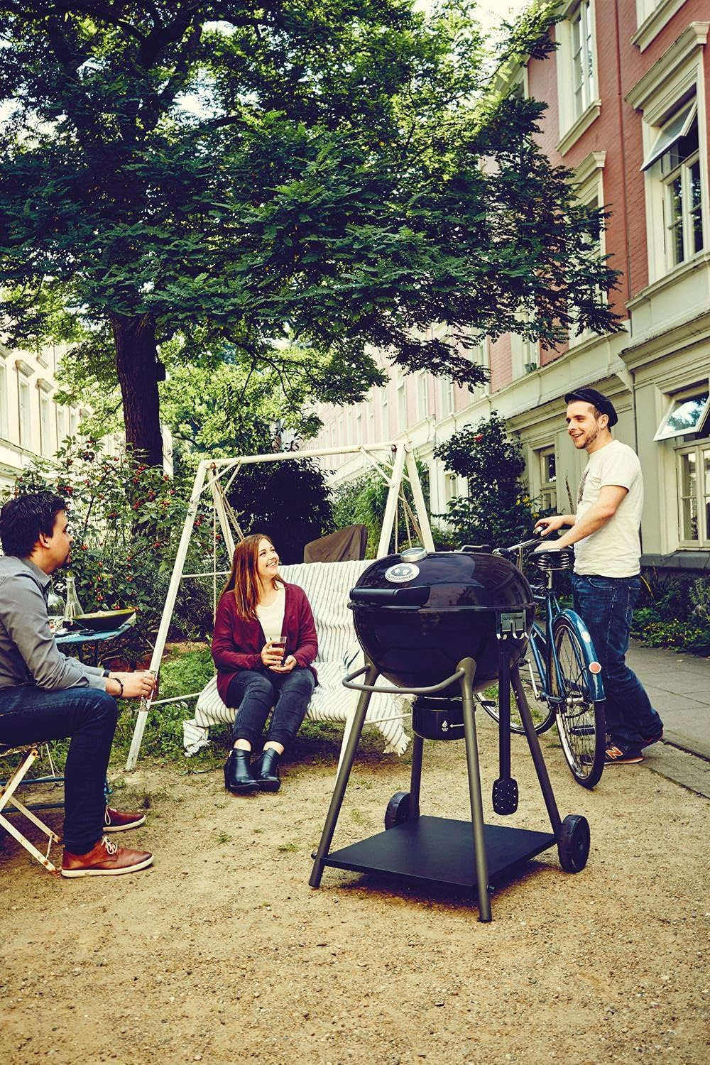 Zwei Männer und eine Frau entspannen sich im Freien mit einem Grill und einem Fahrrad.