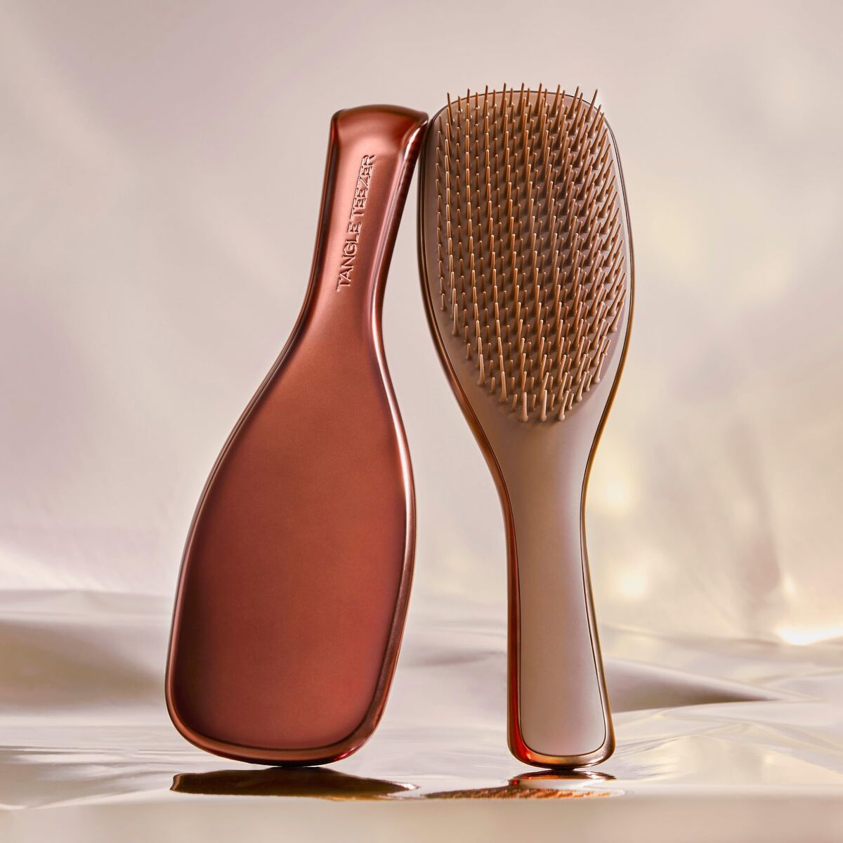 Due spazzole per capelli color oro rosa una accanto all'altra su superficie lucida.