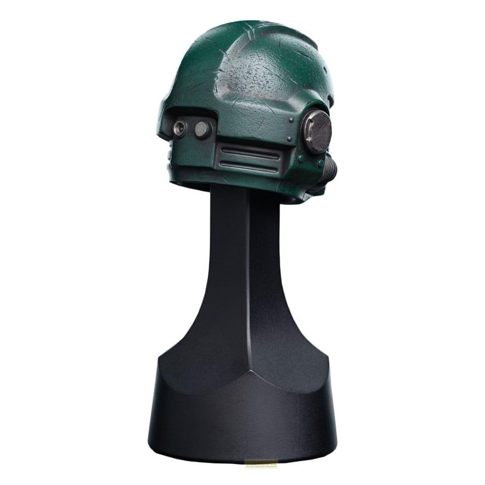 Ein grüner Helm mit Gasmaske auf einem schwarzen Ständer.