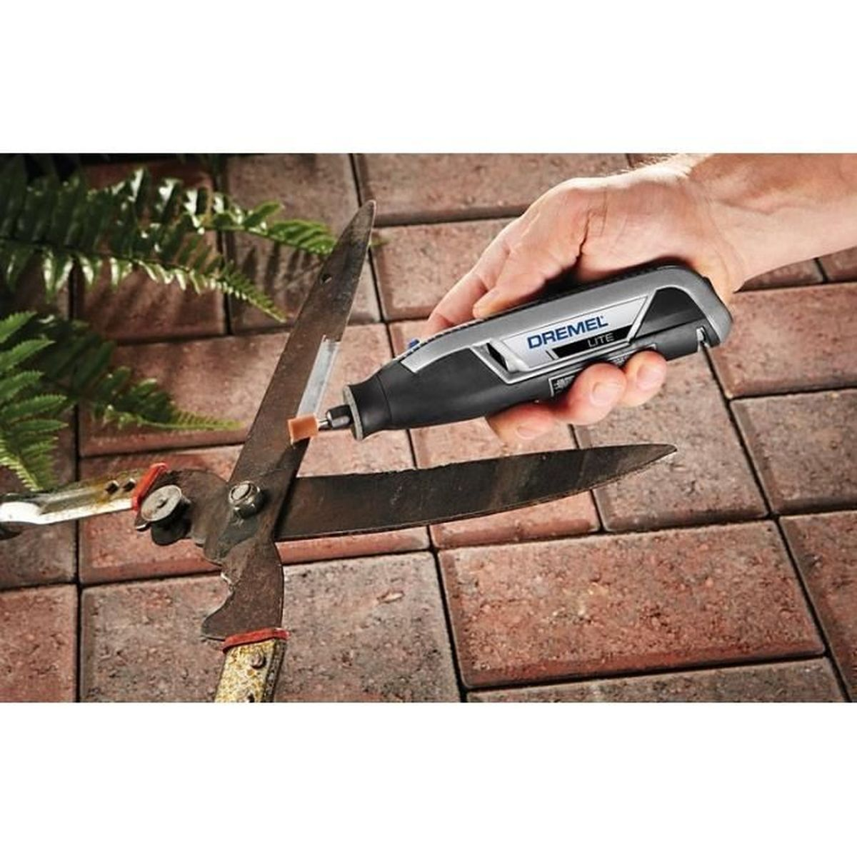 Hand schärft Gartenschere mit Dremel-Werkzeug auf Ziegelsteinboden.