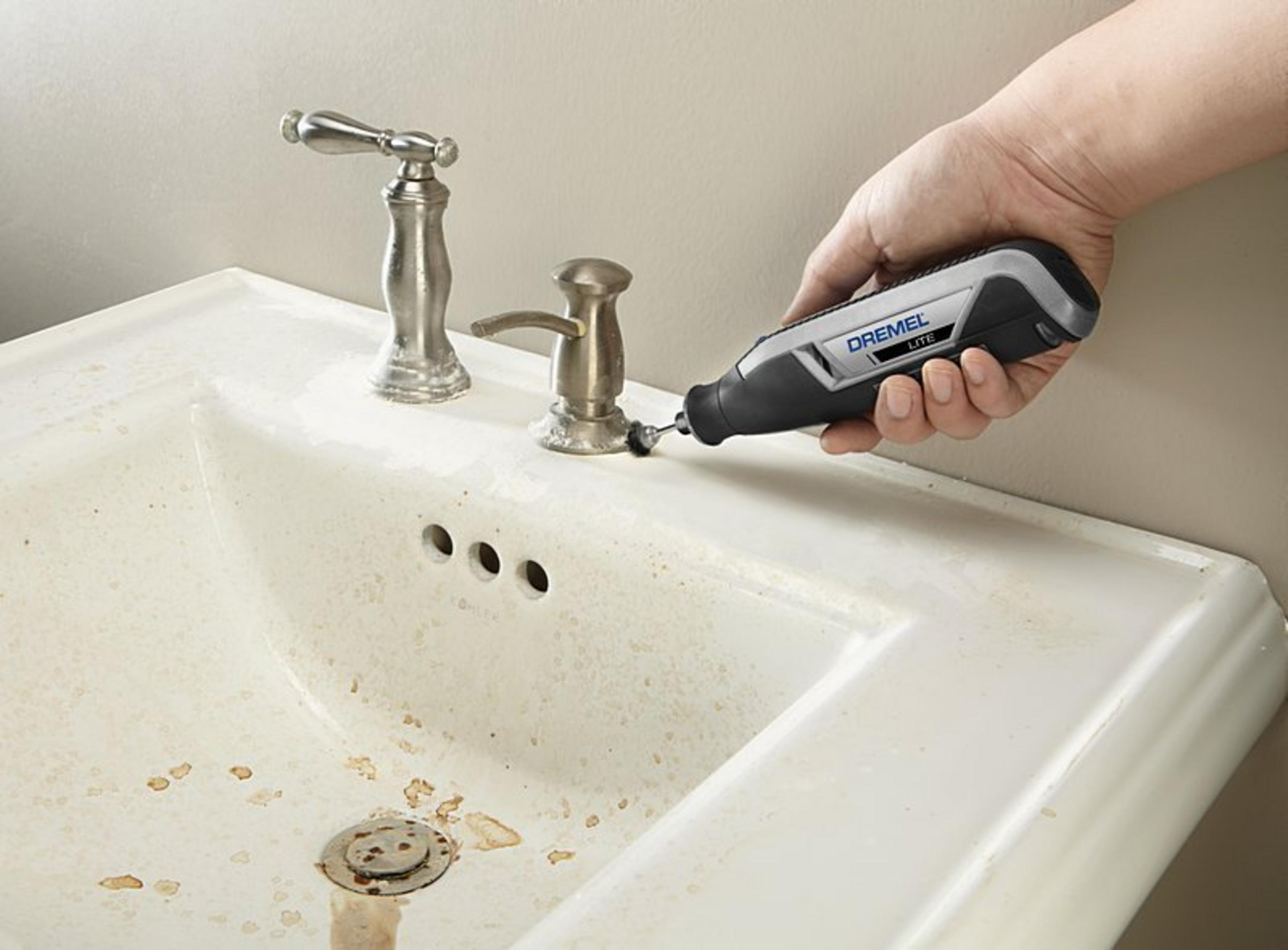 Hand hält Dremel-Werkzeug, das an einem schmutzigen Waschbecken verwendet wird.