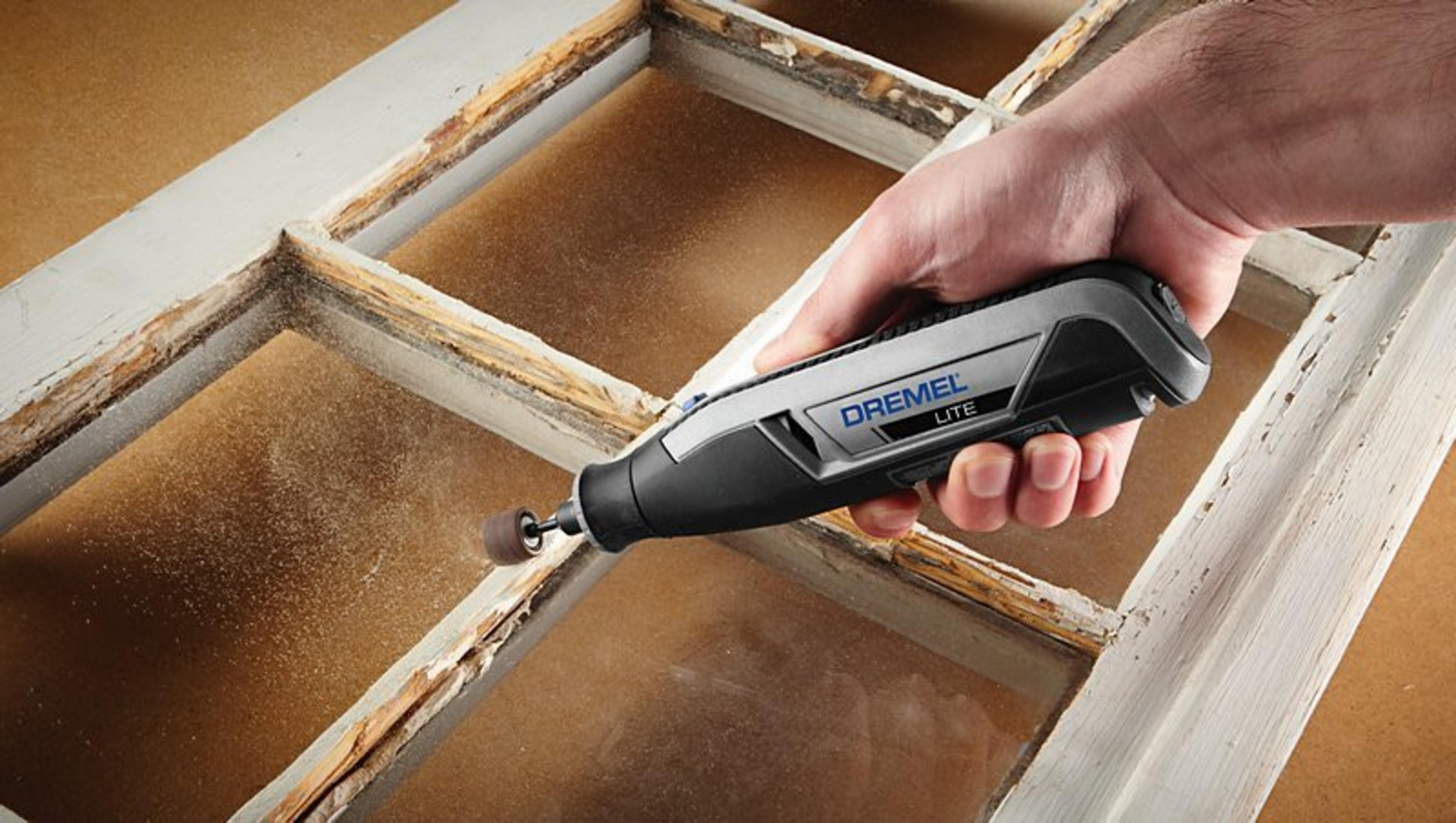 Hand schleift verwittertes Fenster mit Dremel Werkzeug, Staub wirbelt auf.