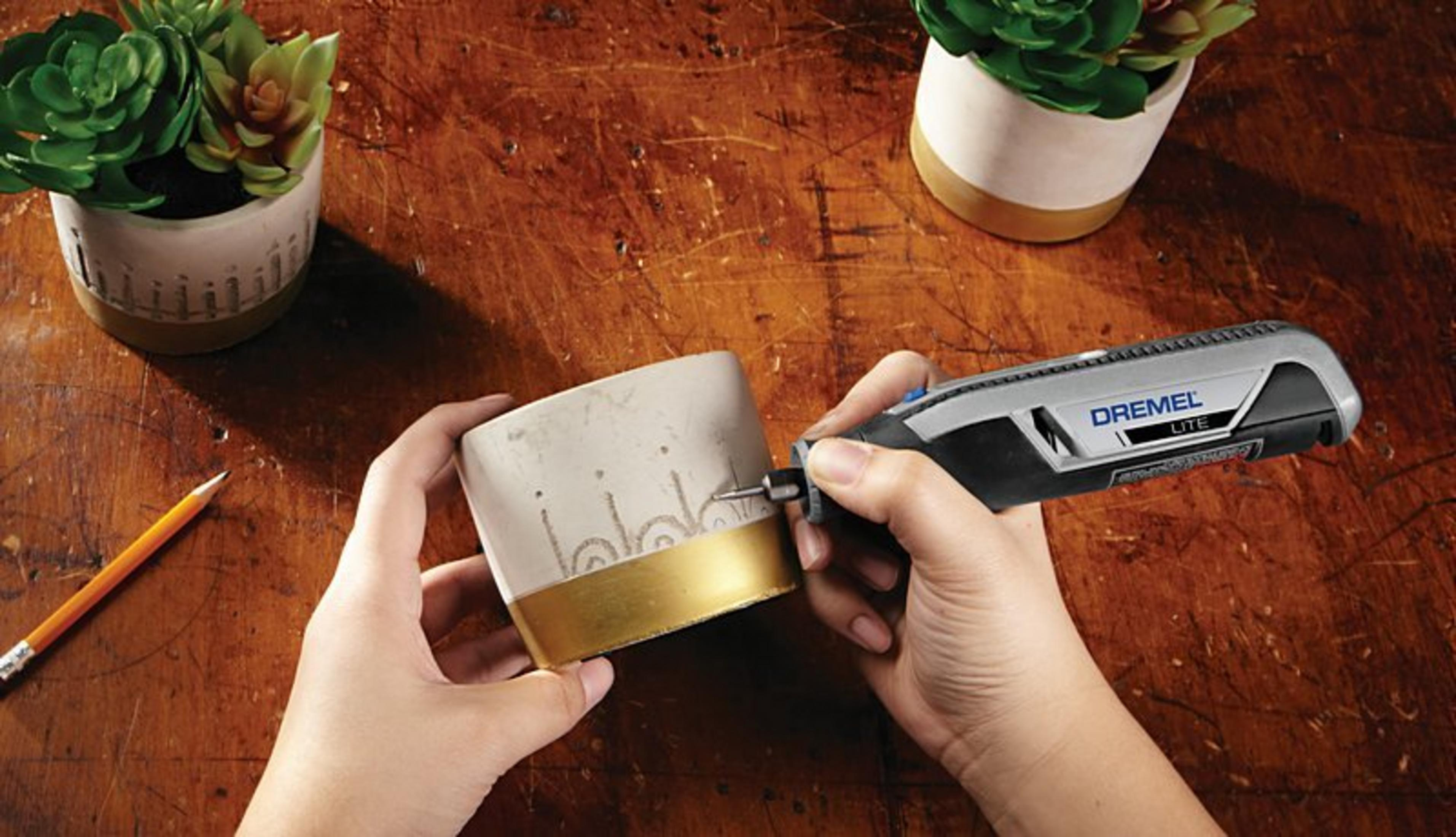 Hände benutzen Dremel Lite Werkzeug zum Ätzen eines Beton topfes mit Goldbasis. Pflanzen in der Nähe.