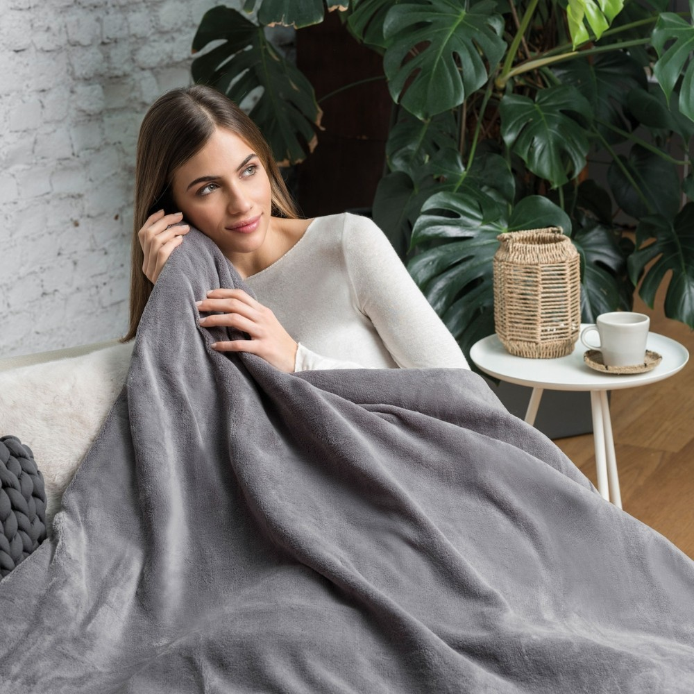 A woman sits on a couch, wrapped in a gray blanket. Cozy scene.