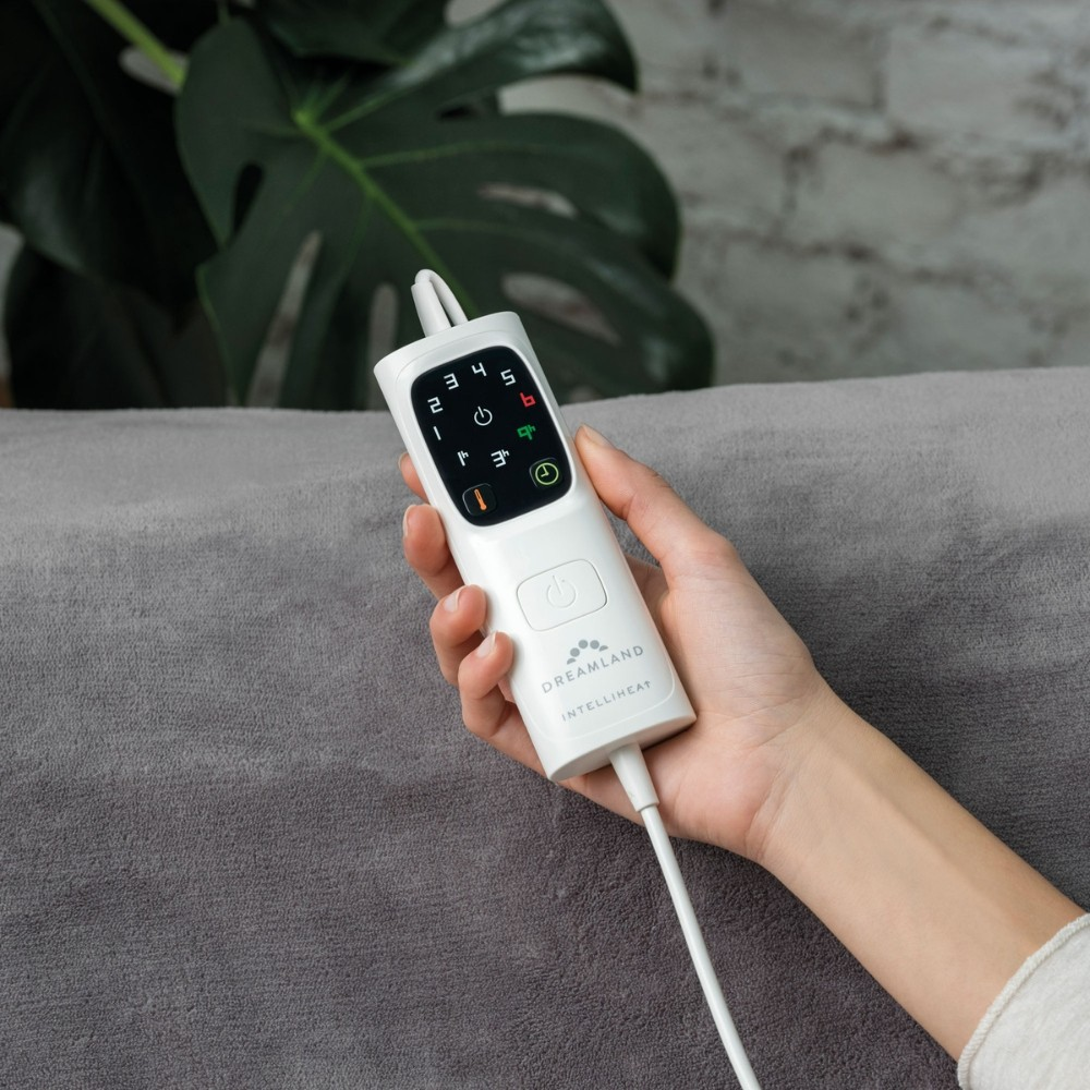 A hand holds a white remote control with a display and buttons.