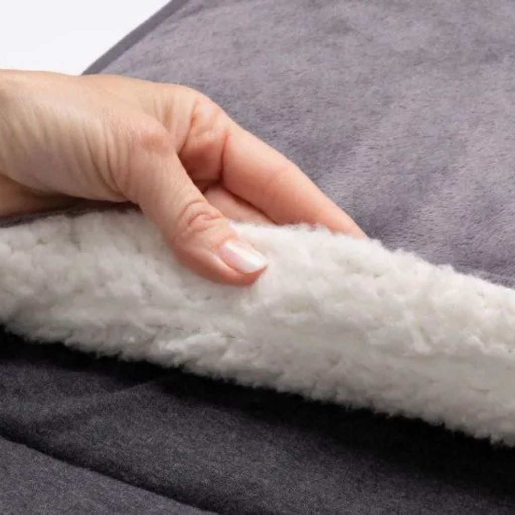A hand touches a soft, grey blanket with white sherpa lining.