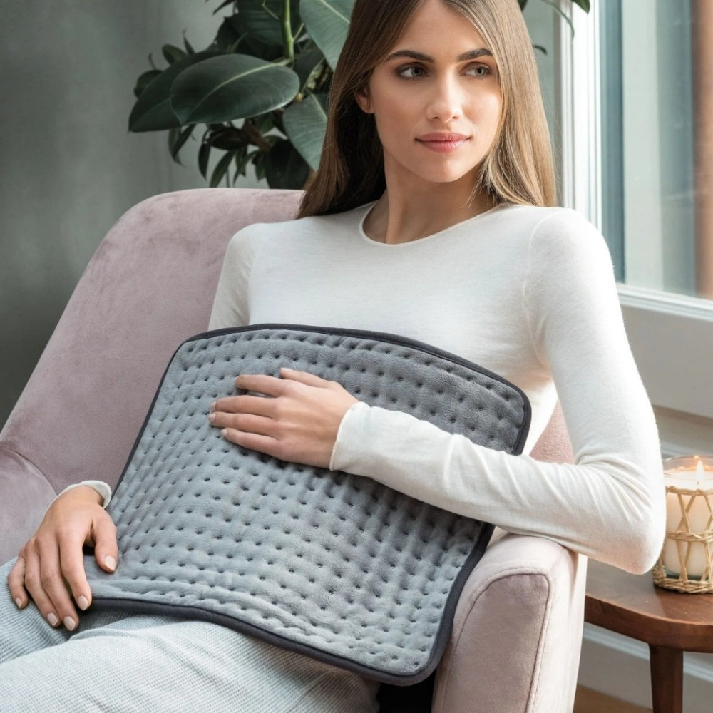 Woman sitting in a chair holding a grey heating pad.