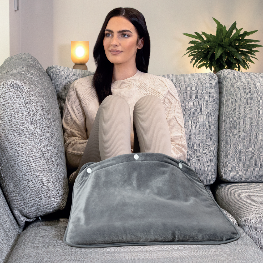Woman sitting on a couch, warming her feet in a grey foot pouch.