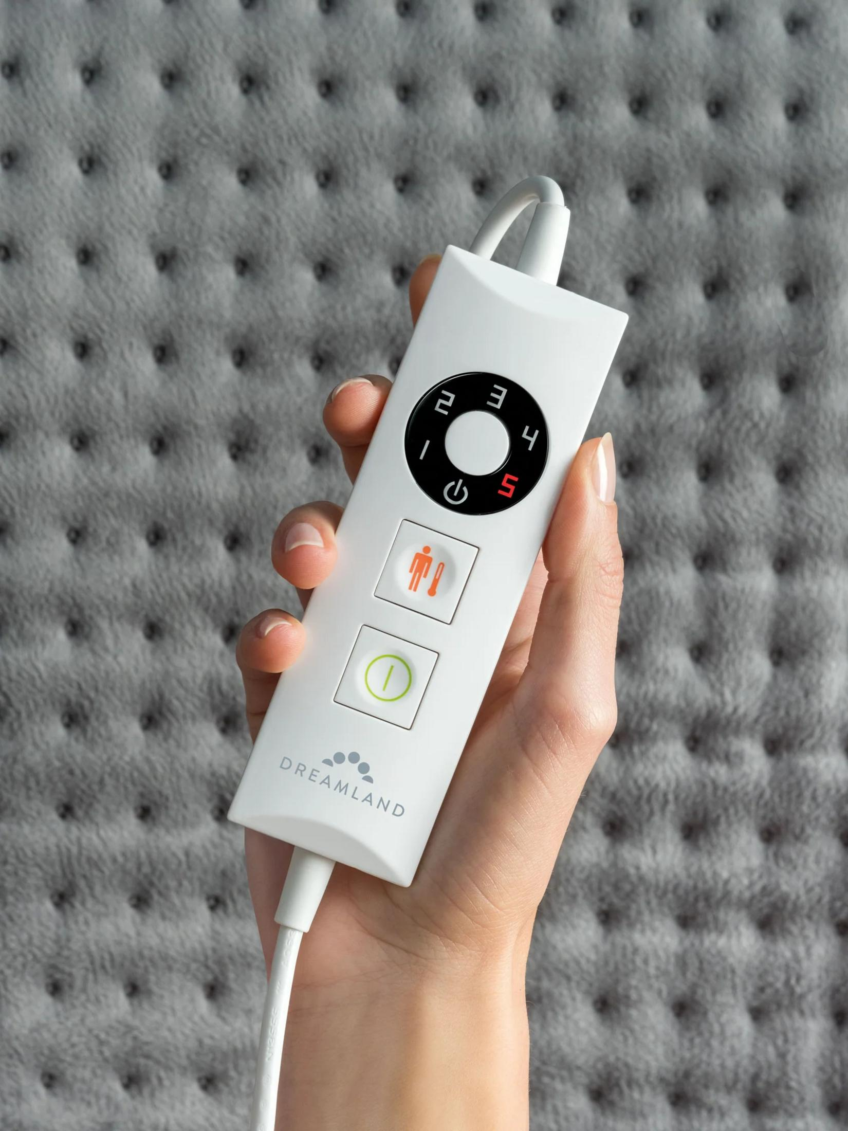 A hand holds a white remote with a digital display against a gray tufted background.