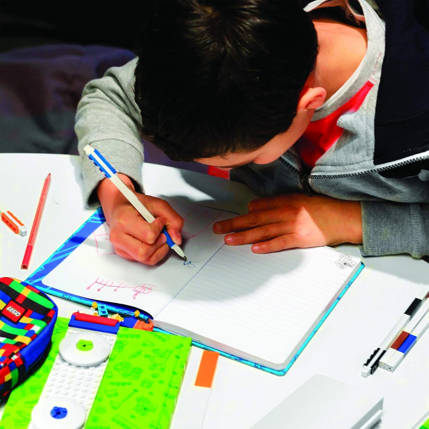 Un ragazzo scrive su un quaderno con matite colorate e accessori LEGO.