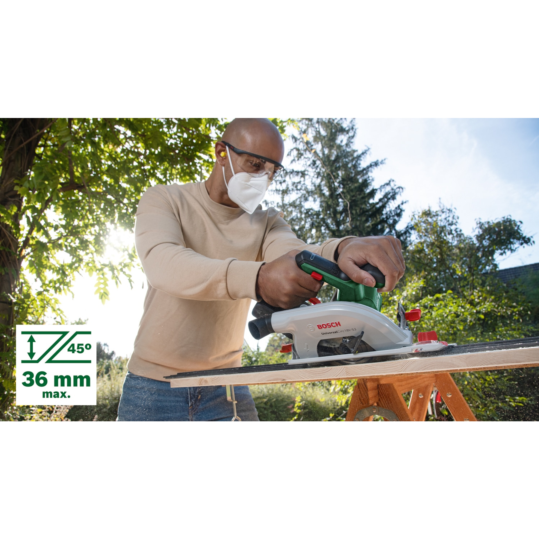 Mann mit Maske und Brille schneidet Holz mit Kreissäge im Freien.