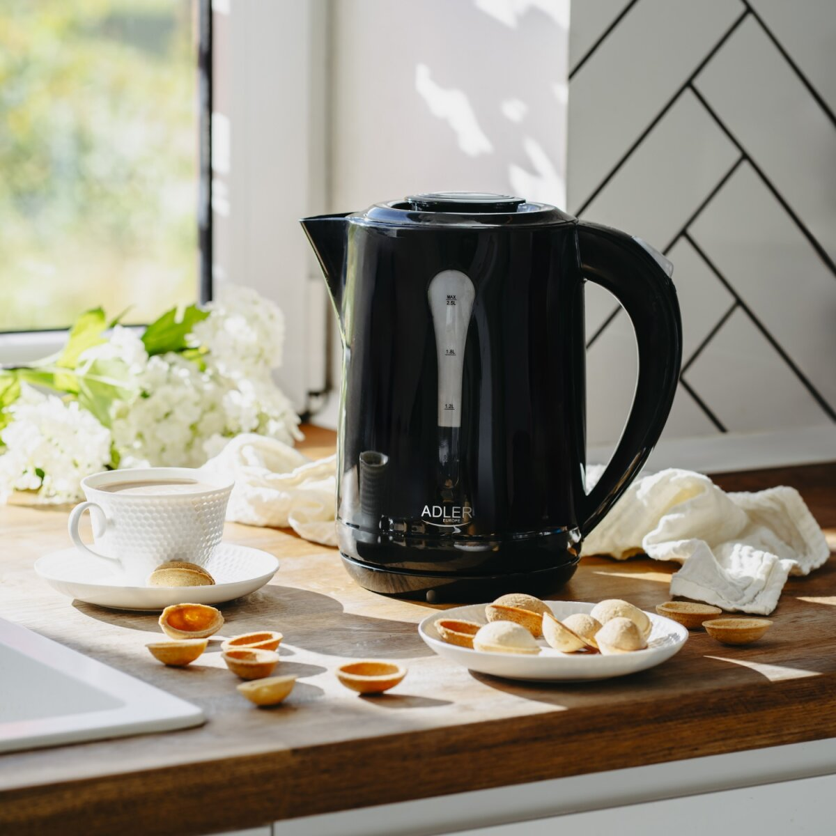 Schwarzer Wasserkocher mit Tasse Kaffee und Keksen auf einem Holztresen.