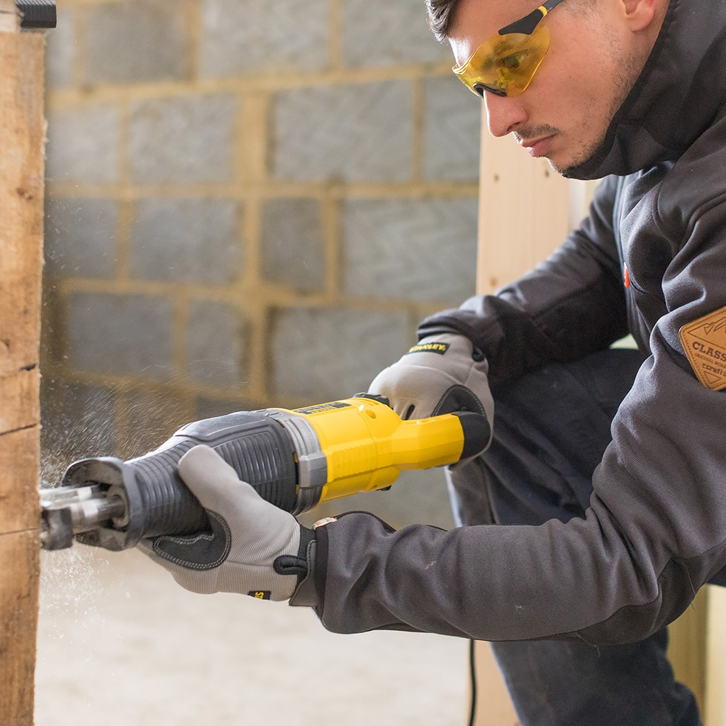 Man in safety glasses saws wood with reciprocating saw, dust flies.