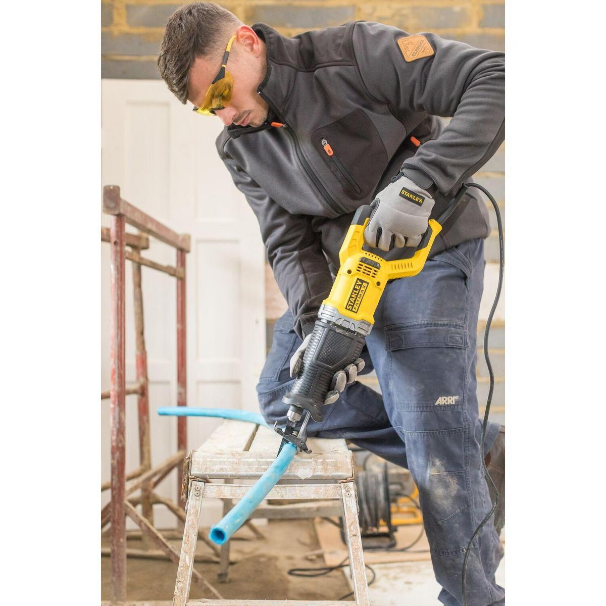 Man in safety glasses saws blue pipe with yellow reciprocating saw.